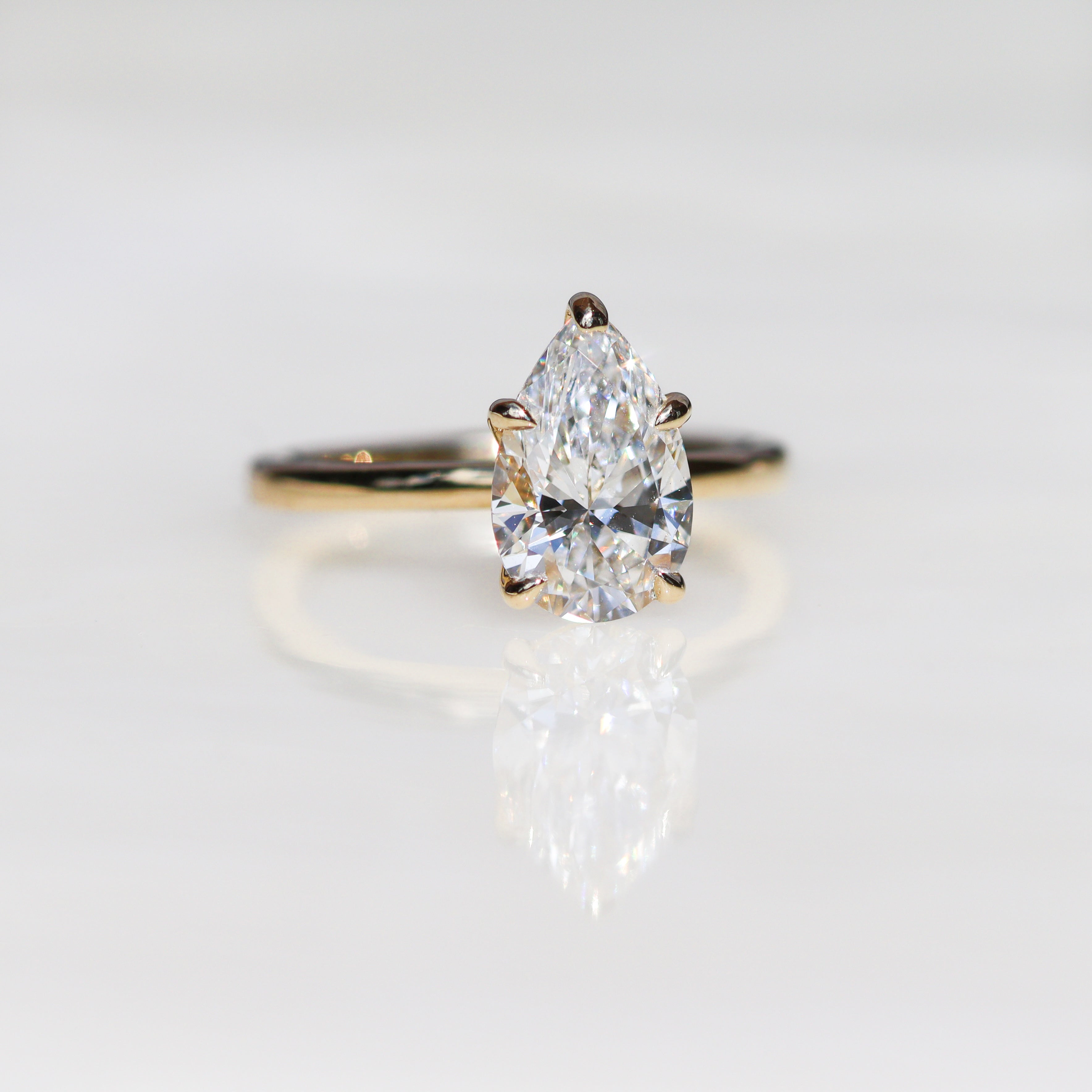 Pear-cut diamond yellow gold ring on white reflective surface.