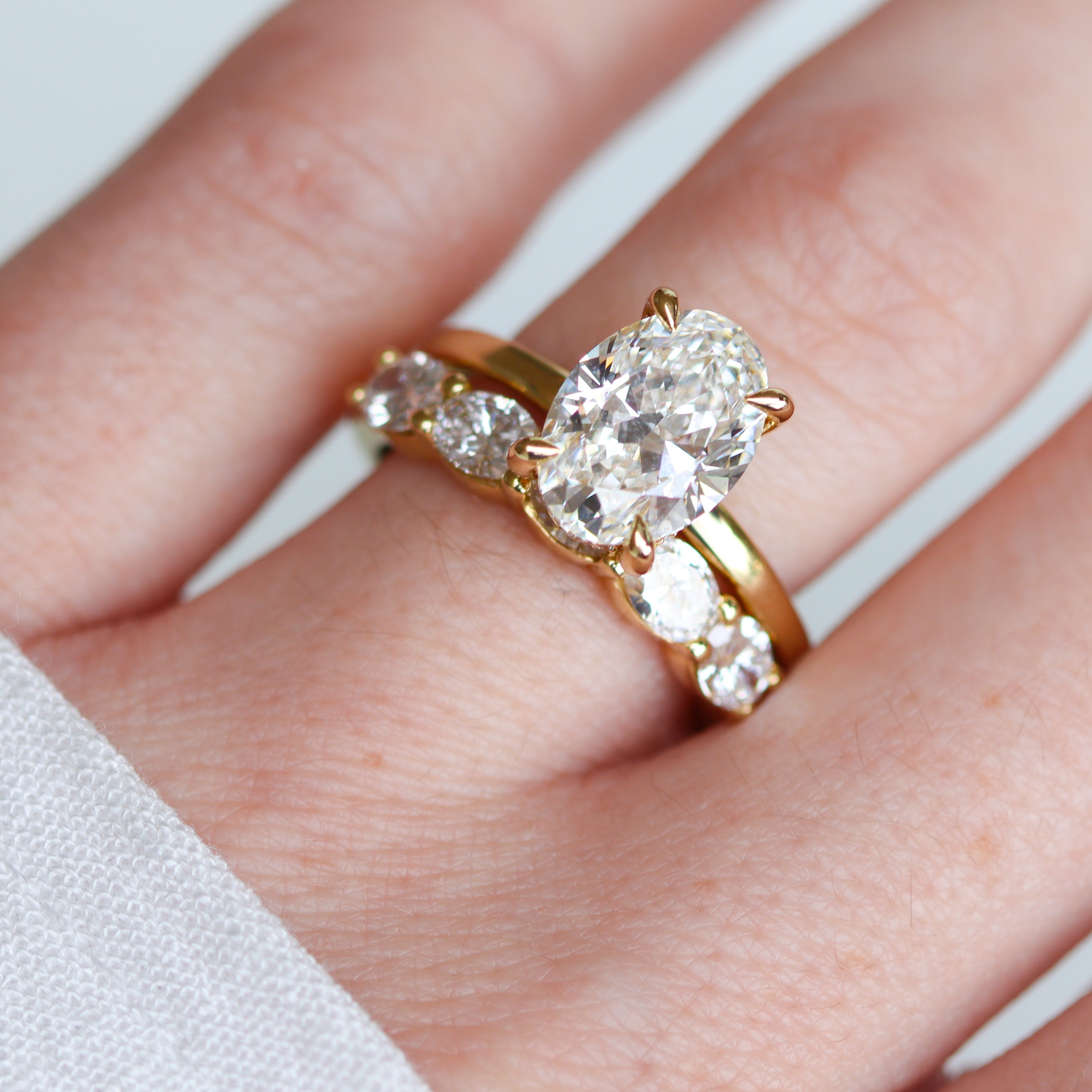 top-down view of 5-Stone oval ring with an oval solitaire engagement ring on a finger
