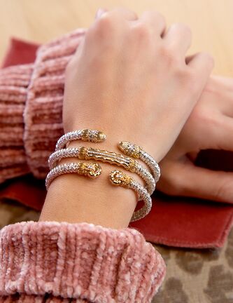 Close-up of a wrist wearing multiple gold and silver bracelets with a pink textured sleeve.