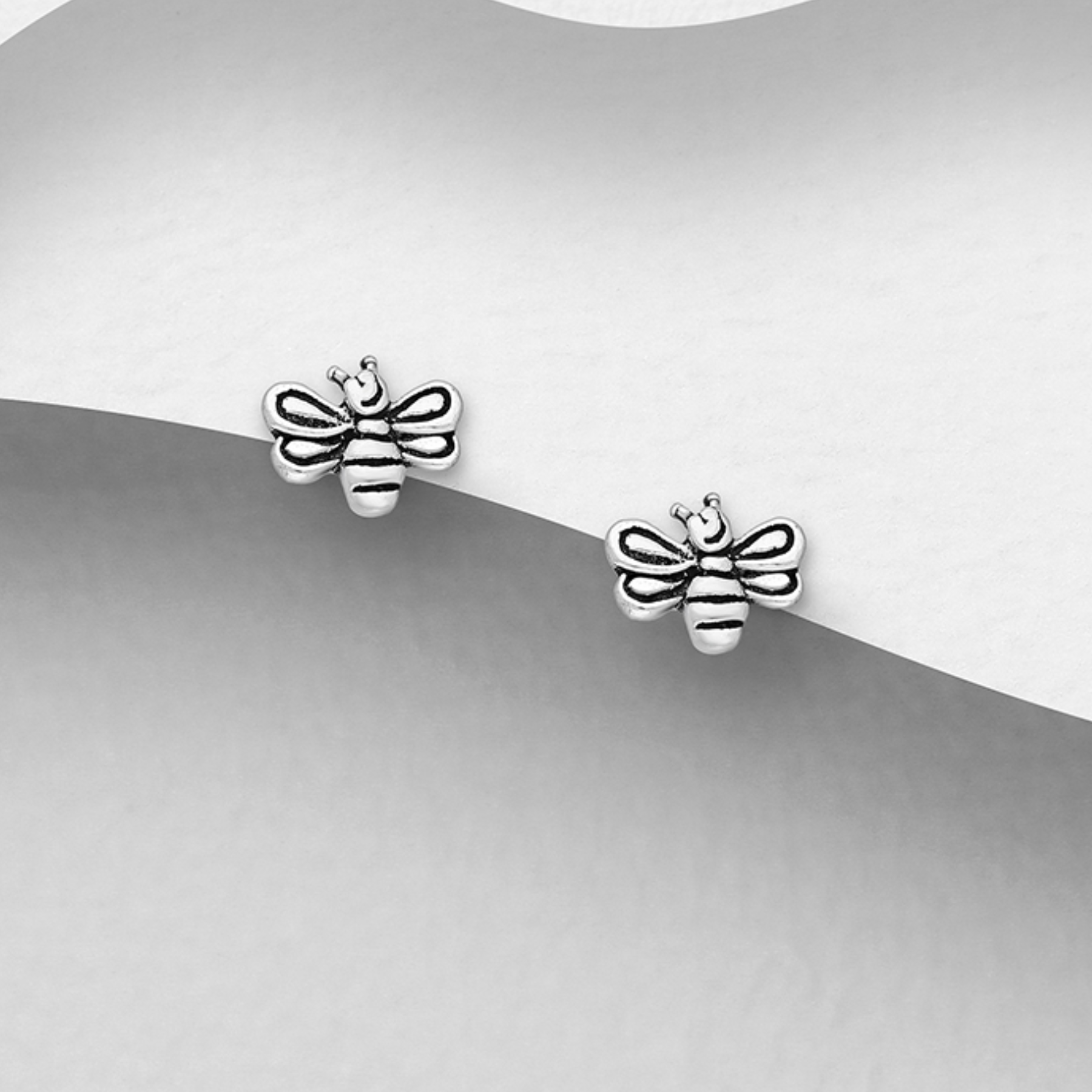 Silver bee-shaped earrings on a gray and white background
