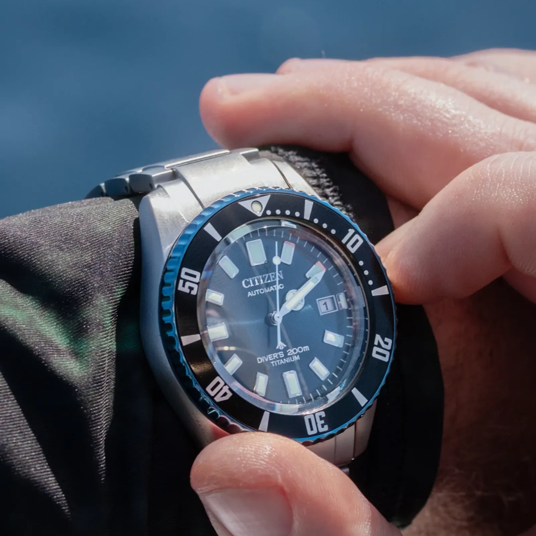 Person wearing a Citizen watch with a blue and black dial, holding it against a blurred natural background.