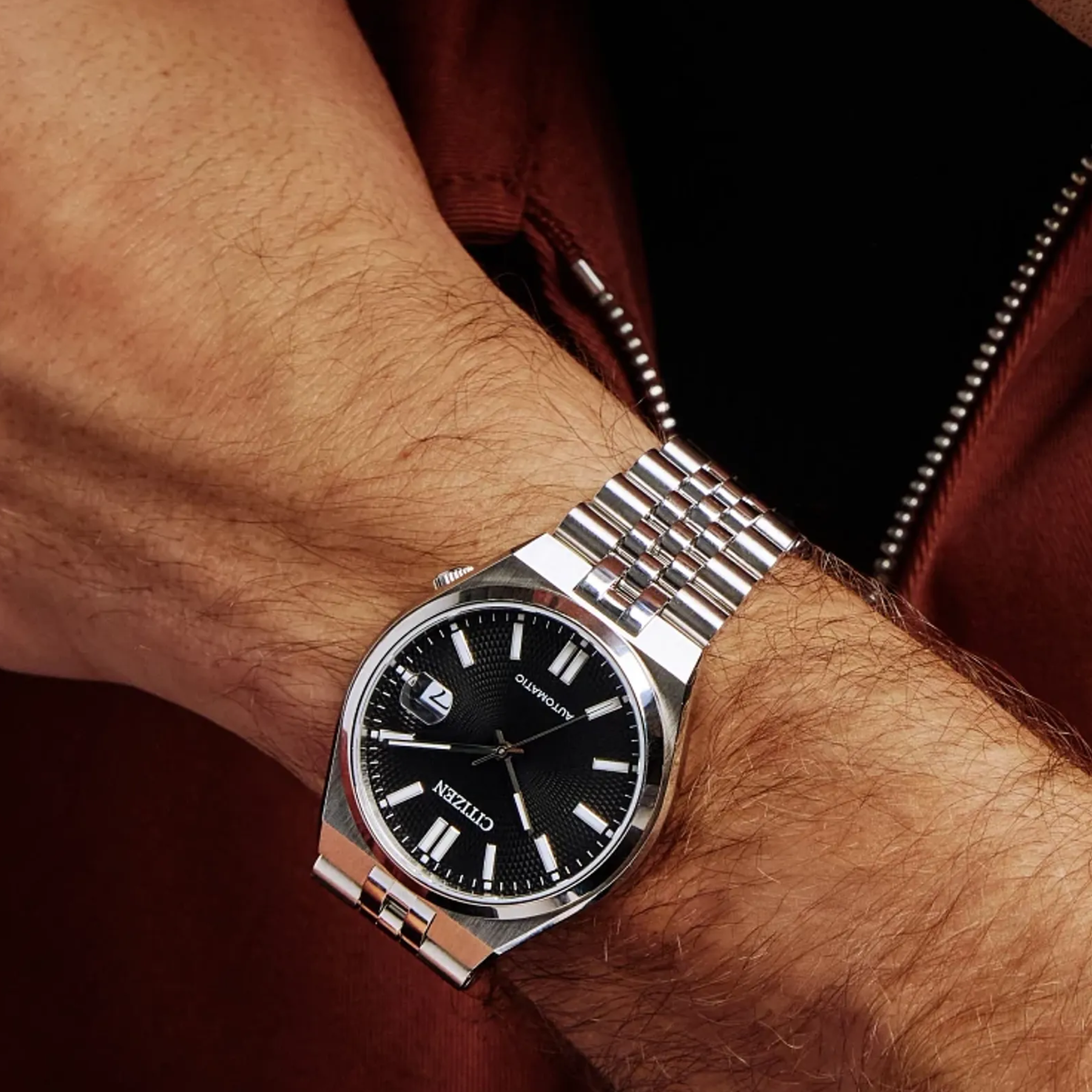Silver watch with black dial on a wrist against a dark background