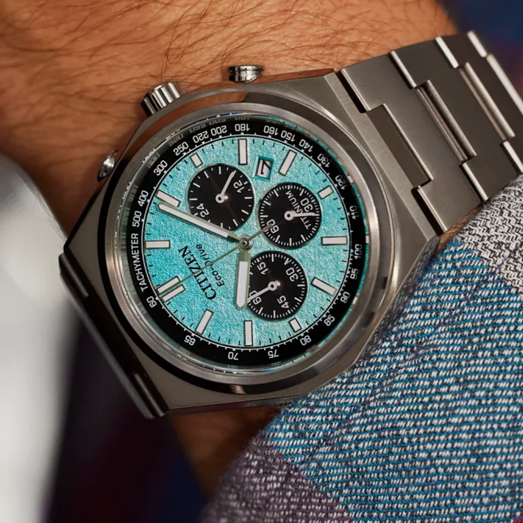 Silver watch with a blue face on a wrist against a denim background