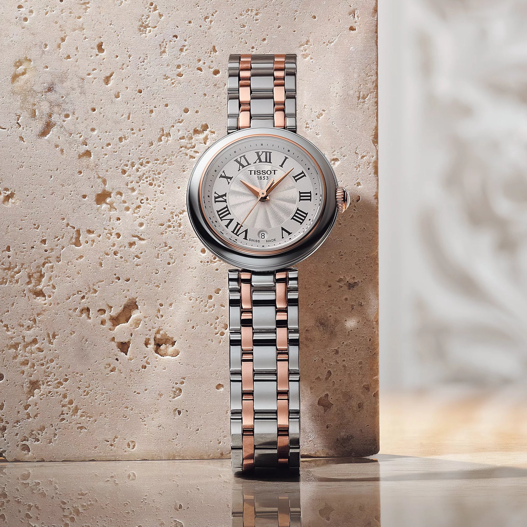 Tissot watch with silver and rose gold band on a textured surface