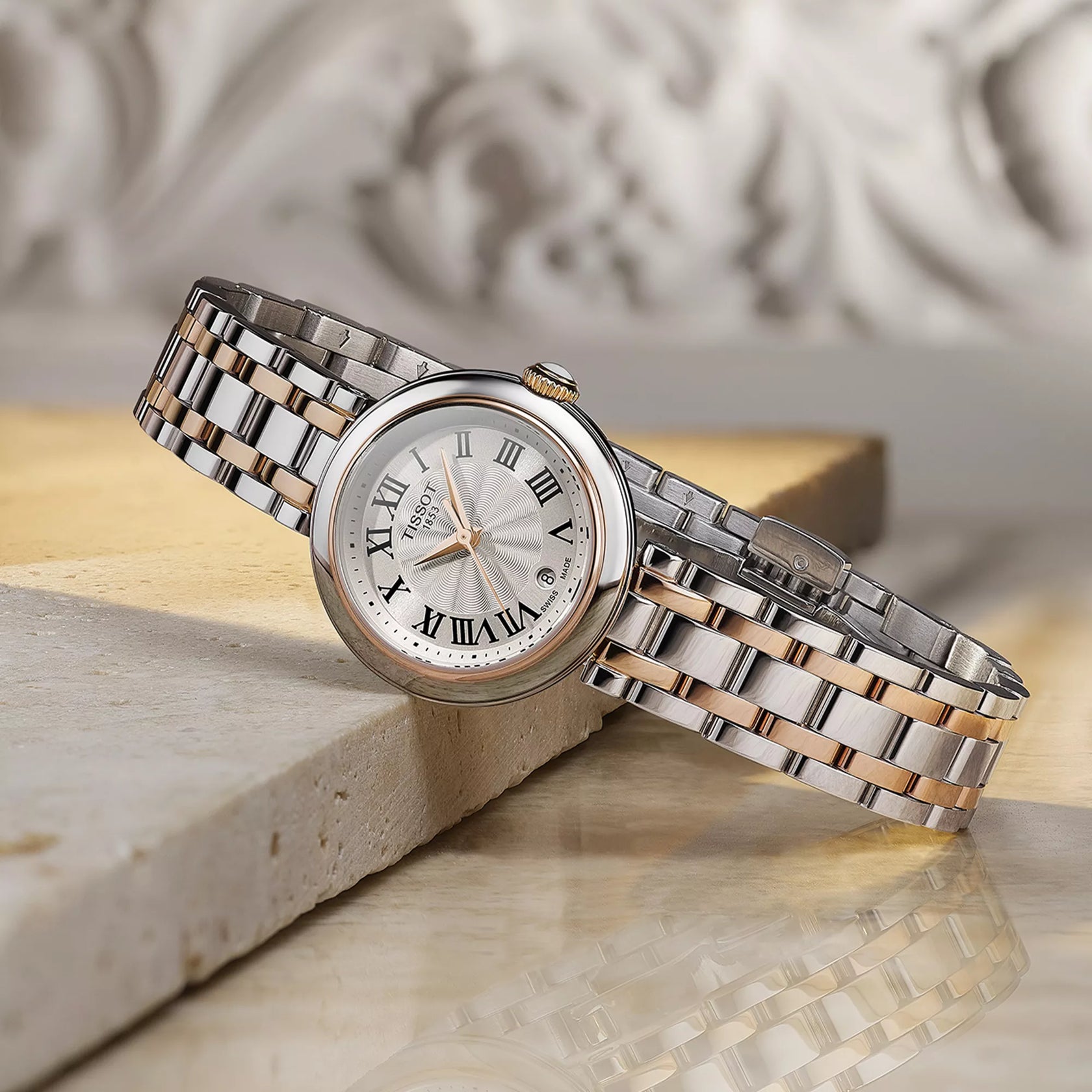 Silver and rose gold watch with Roman numeral markers on a marble surface
