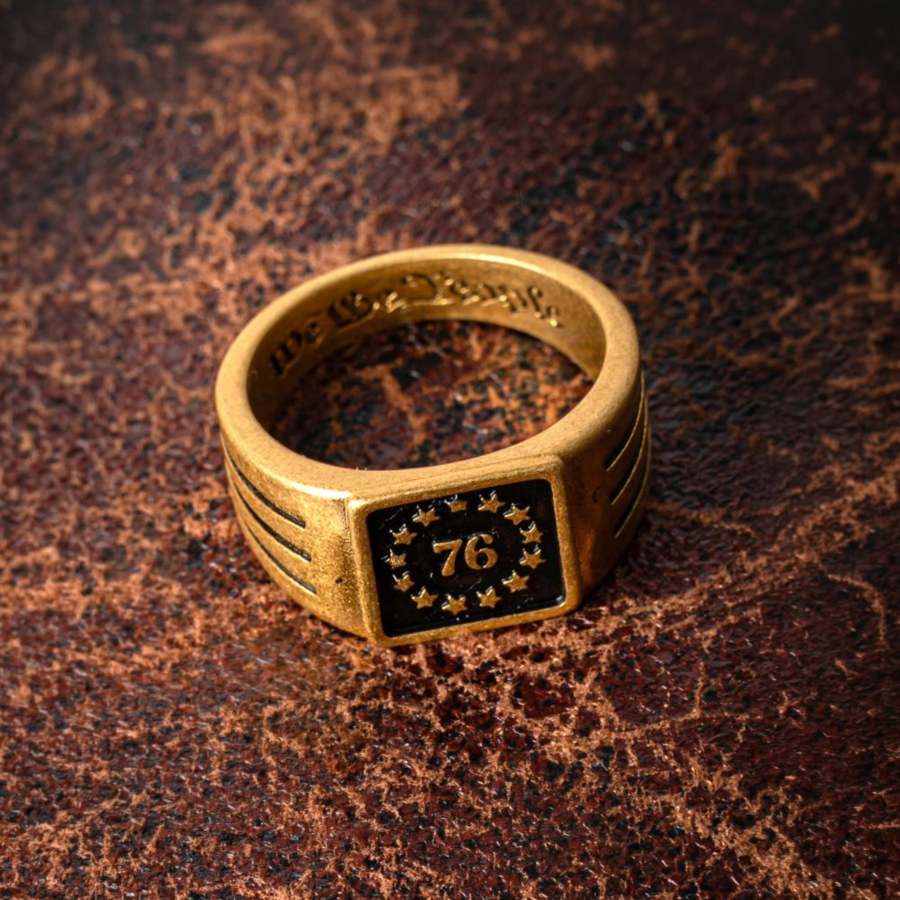 Gold ring with a black square emblem featuring the number 76 on a brown textured background