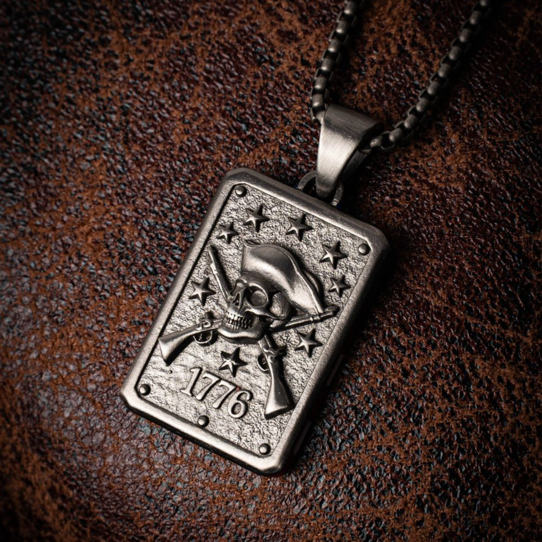 Silver pendant with a skull and crossbones design on a brown leather background