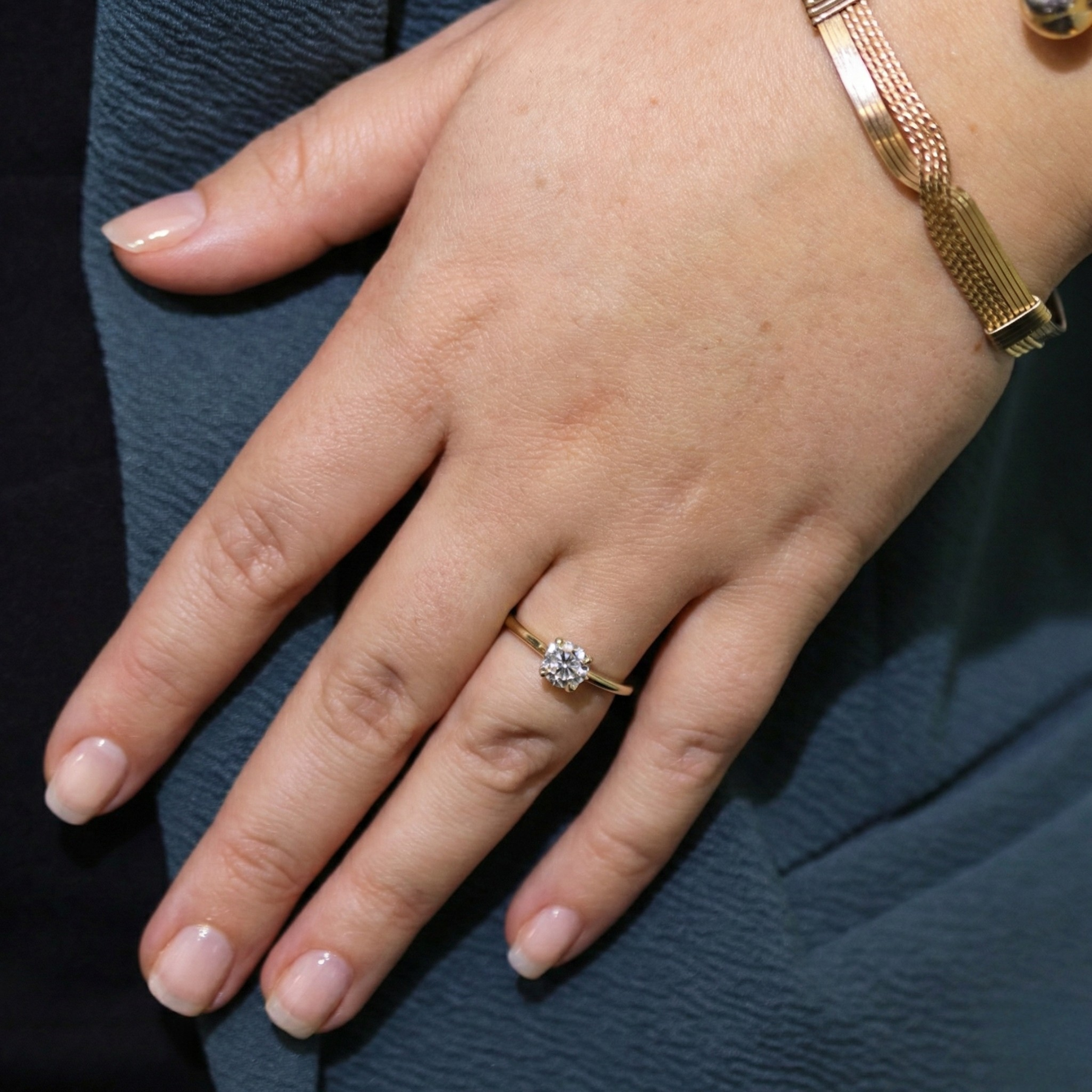 Hand wearing a gold ring with a diamond on a dark background
