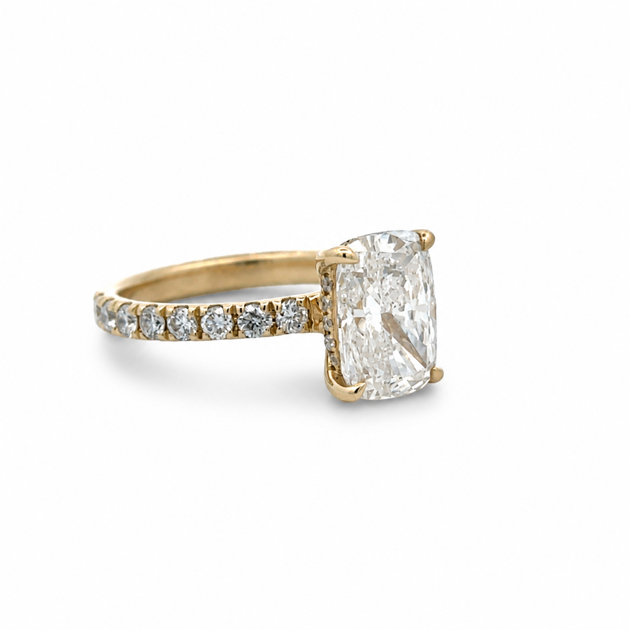 A yellow gold engagement ring featuring a large cushion-cut diamond center stone and a pavé band with small round diamonds, set against a plain white background.