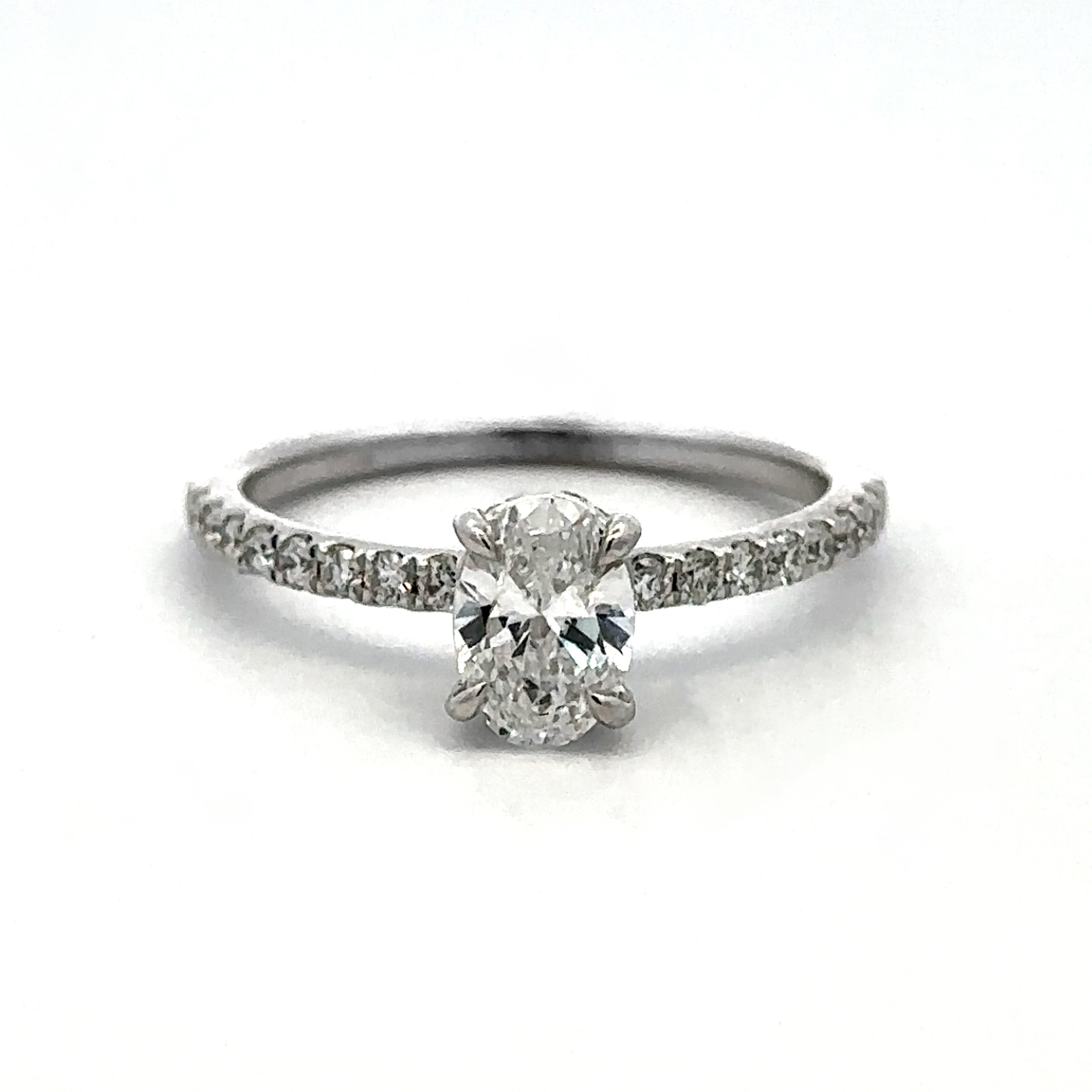 A silver-toned diamond ring featuring a round-cut center stone and a pavé-set band, photographed on a clean white background.
