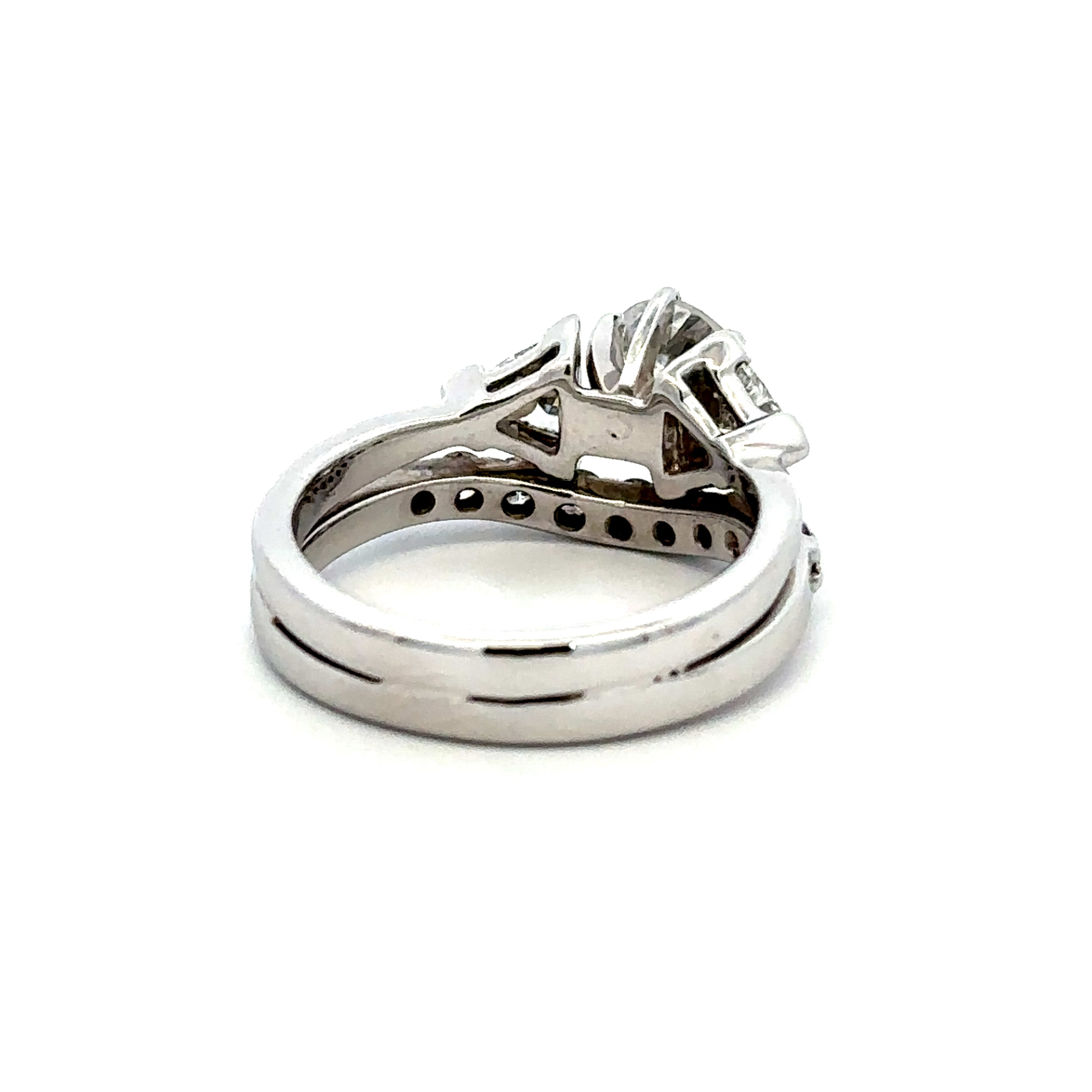 A silver-colored diamond ring with a brilliant round center stone and baguette side stones, shown in a side profile view on a white background.