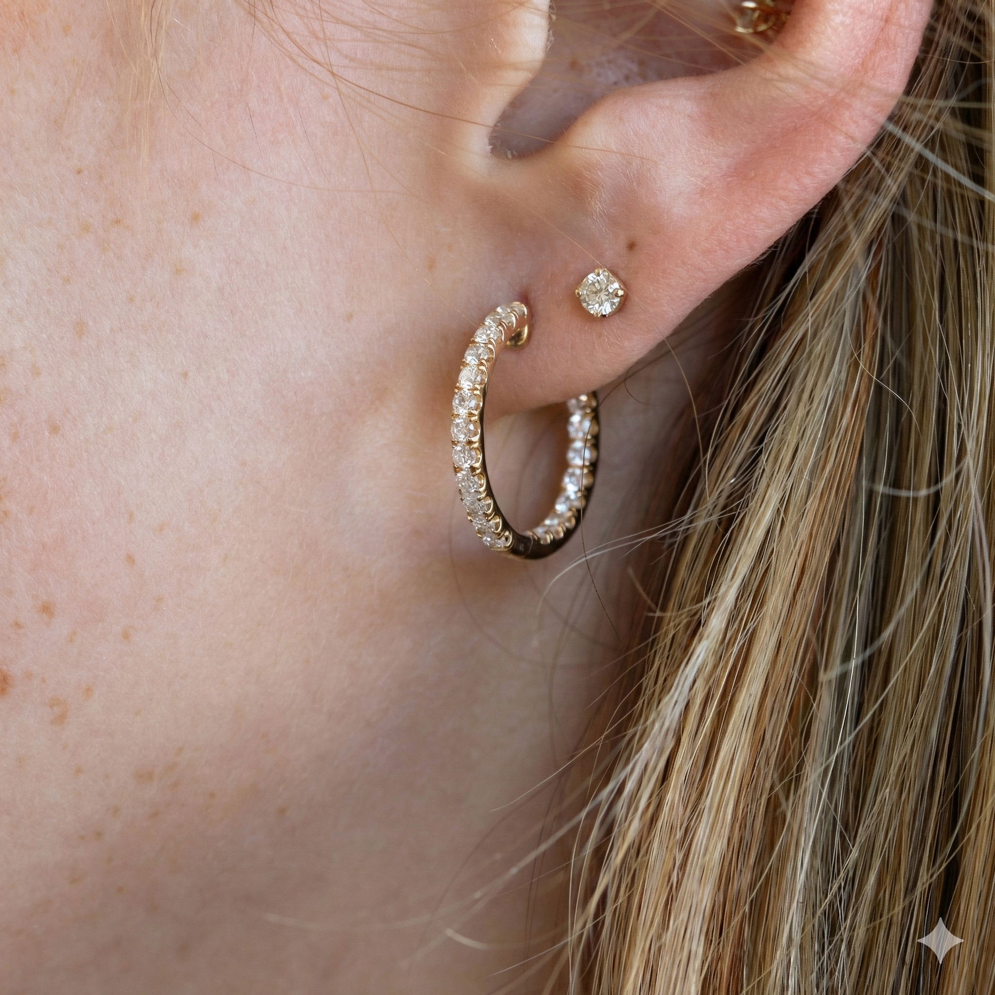 Close-up of an ear wearing a gold hoop earring with small diamonds.