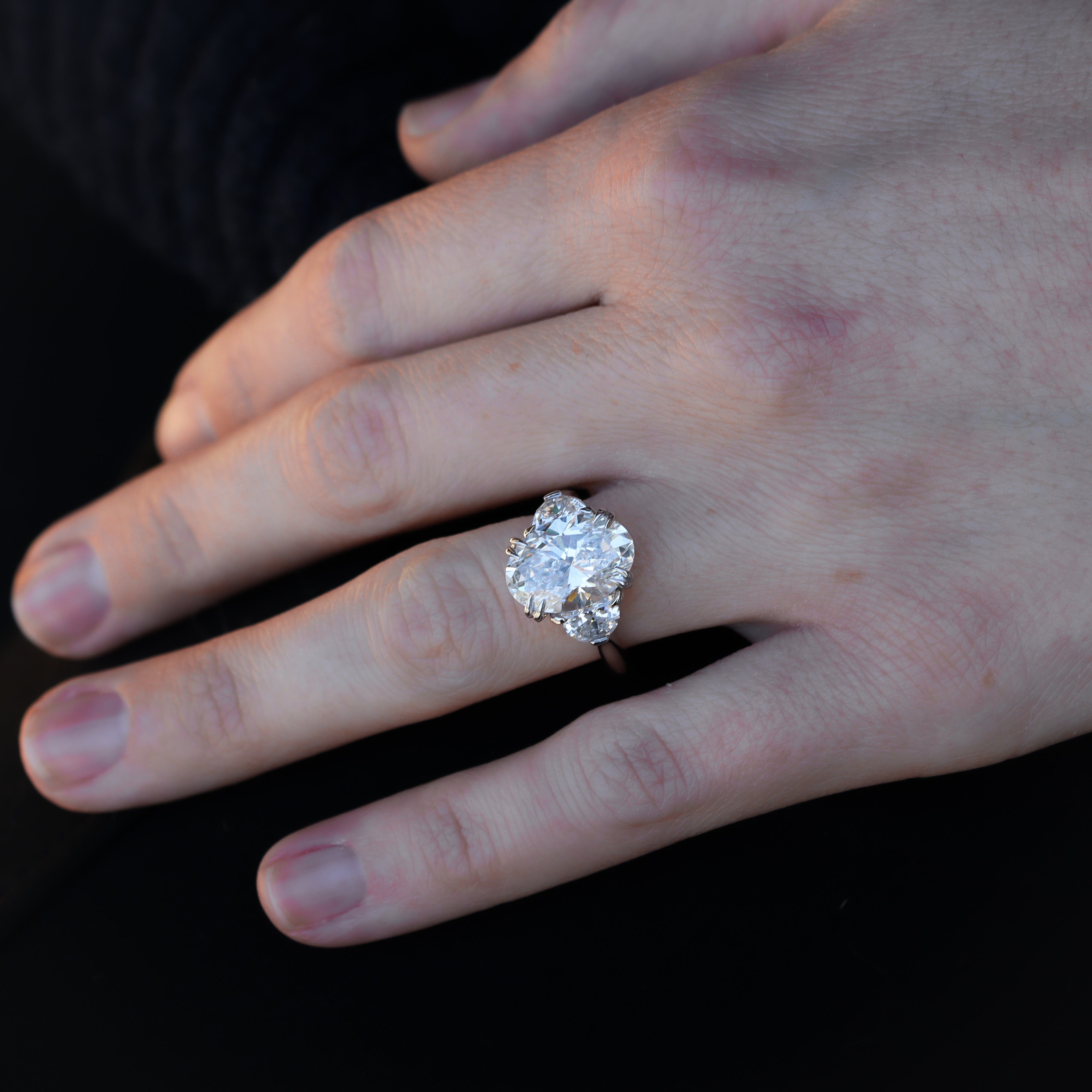 Hand wearing a diamond ring on a dark background