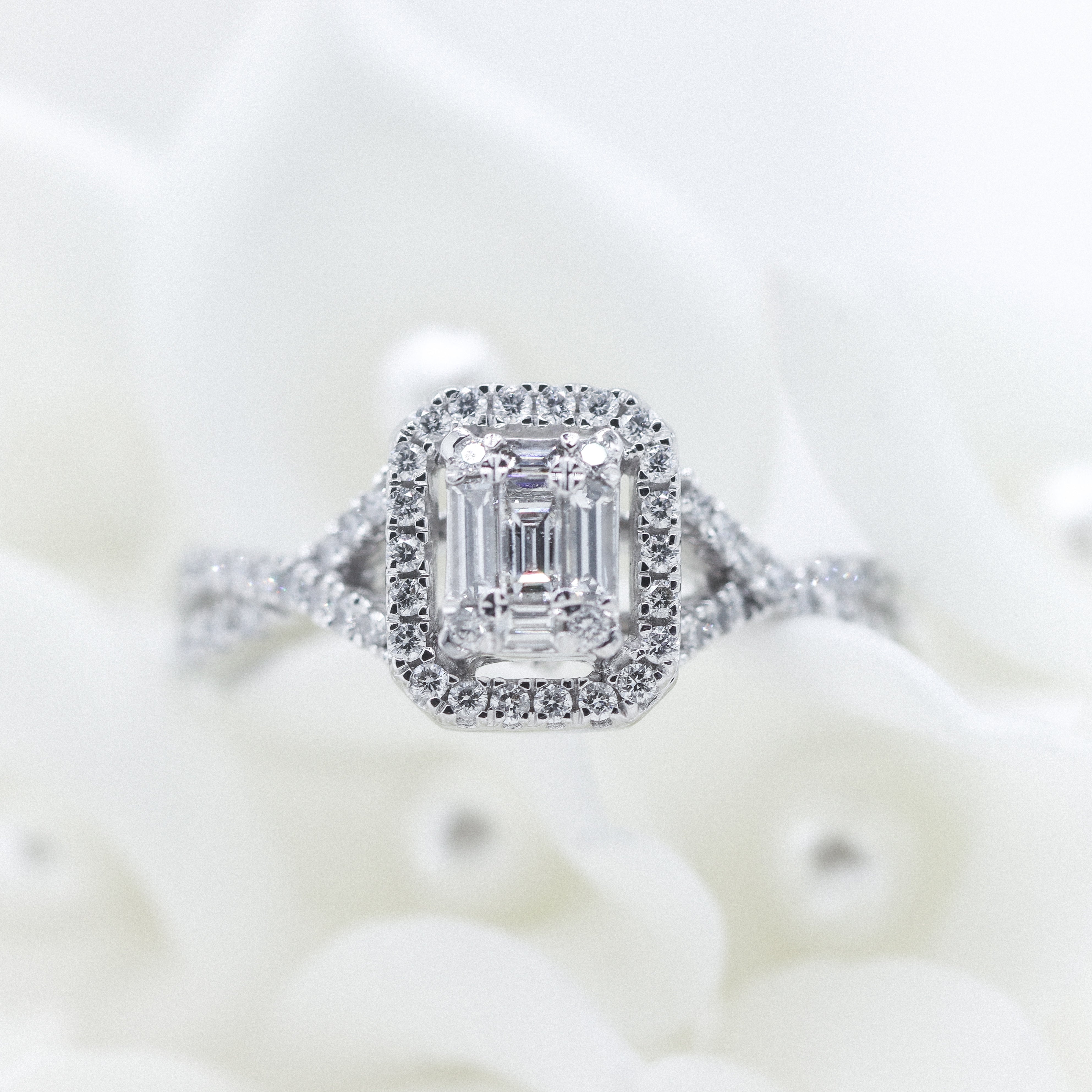 10K White Gold 5/8CTW. Diamond Baguette Halo-Accented Twisted Shank Engagement Ring Sitting in a bouquet of white flowers