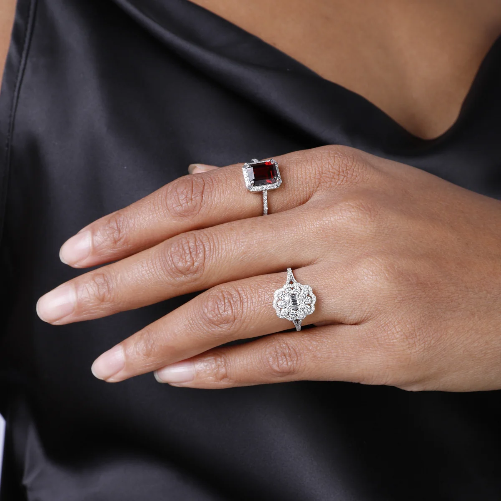 Close-up of a hand wearing two silver rings with gemstones on a black background