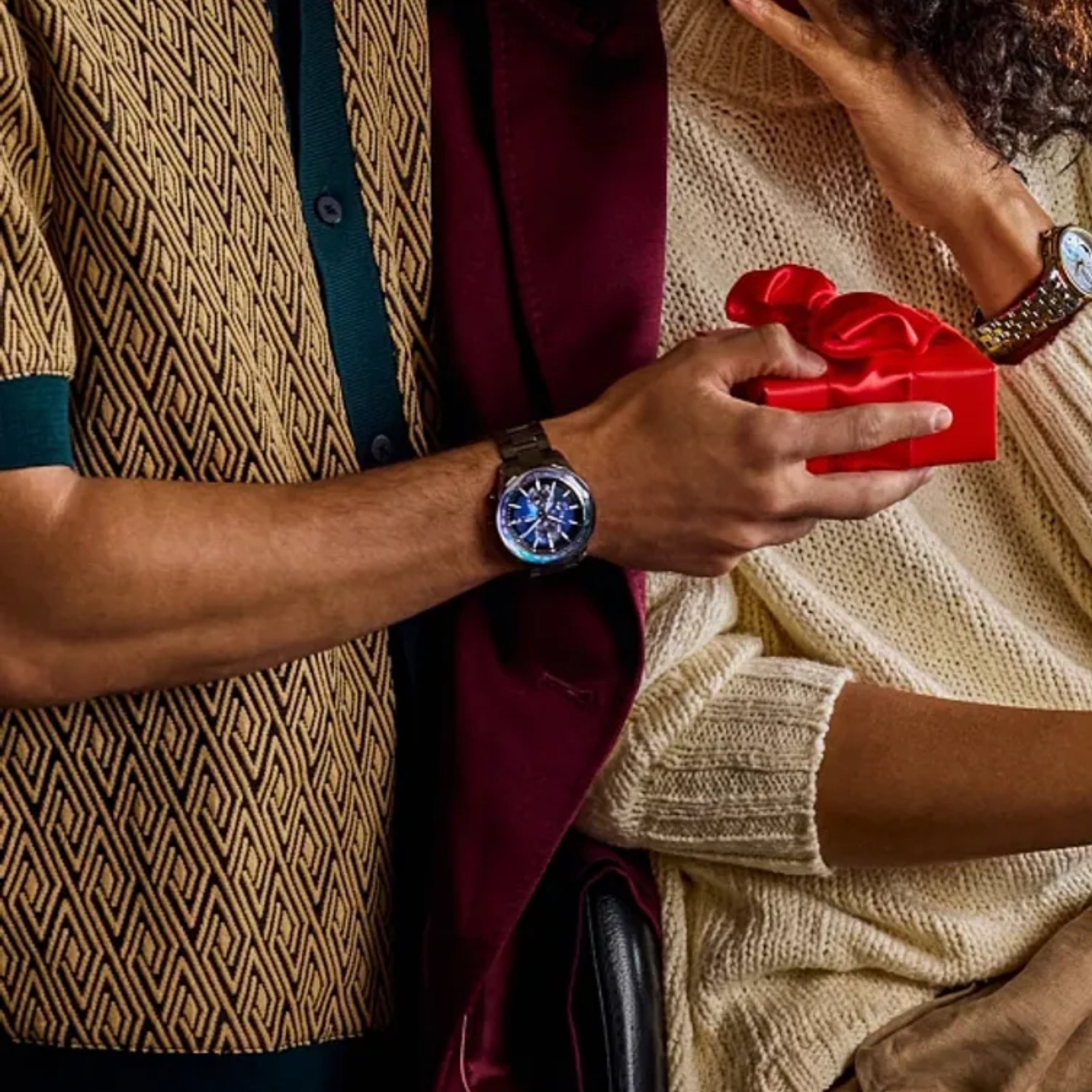 Person holding a red heart-shaped box, likely a gift, with another person wearing a watch.