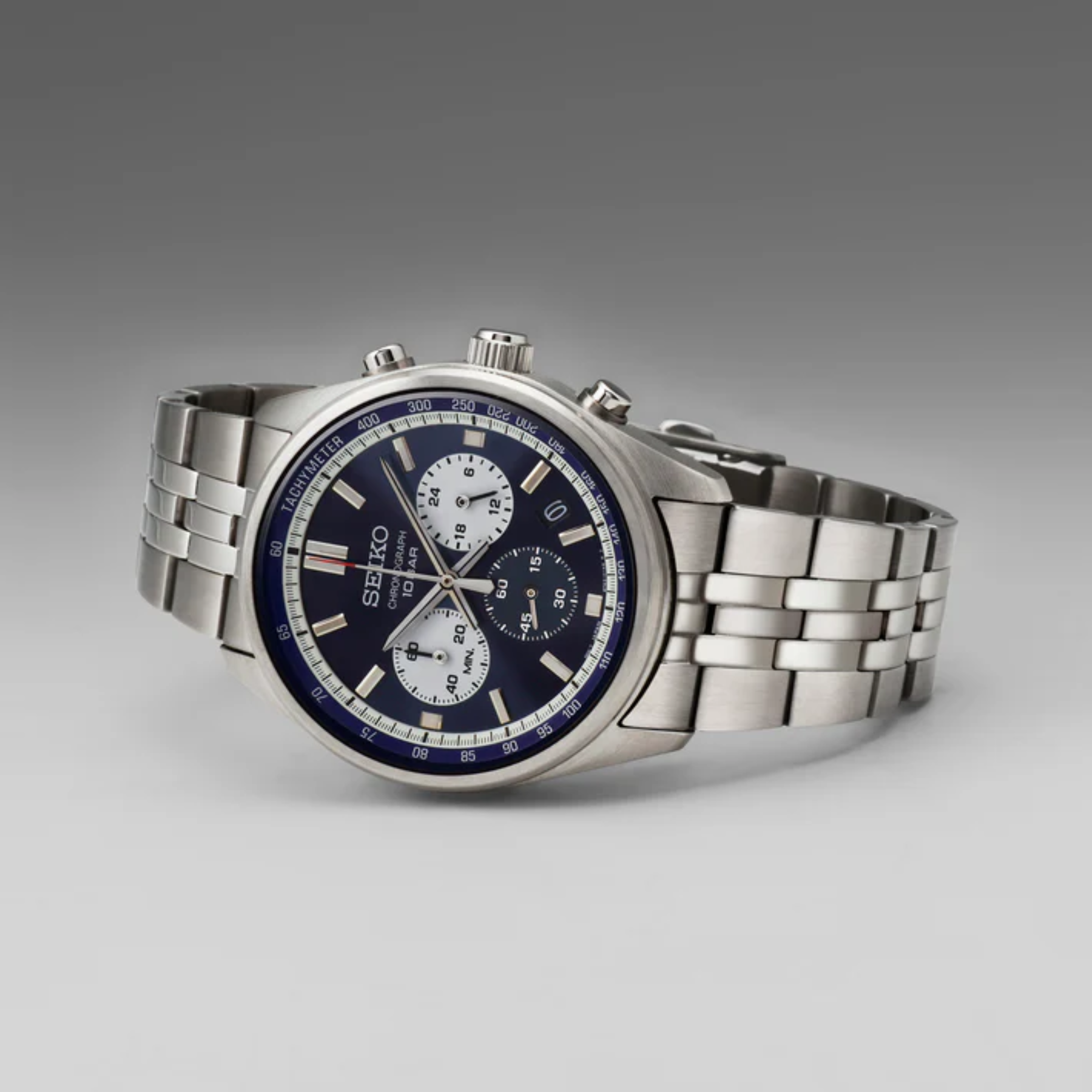 A Seiko stainless steel chronograph watch with a dark blue dial and white subdials, displayed on a neutral gray gradient background.