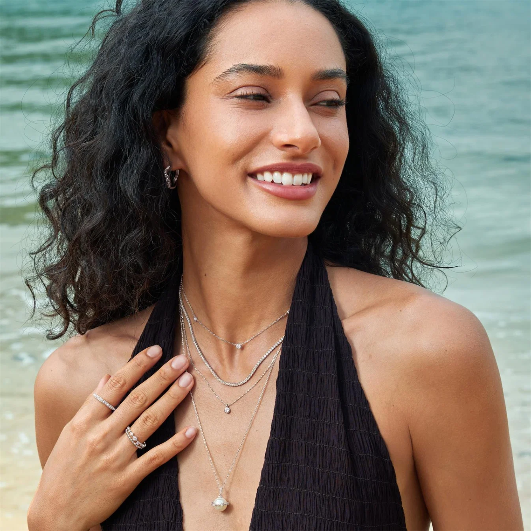Woman wearing layered necklaces and a ring on a beach