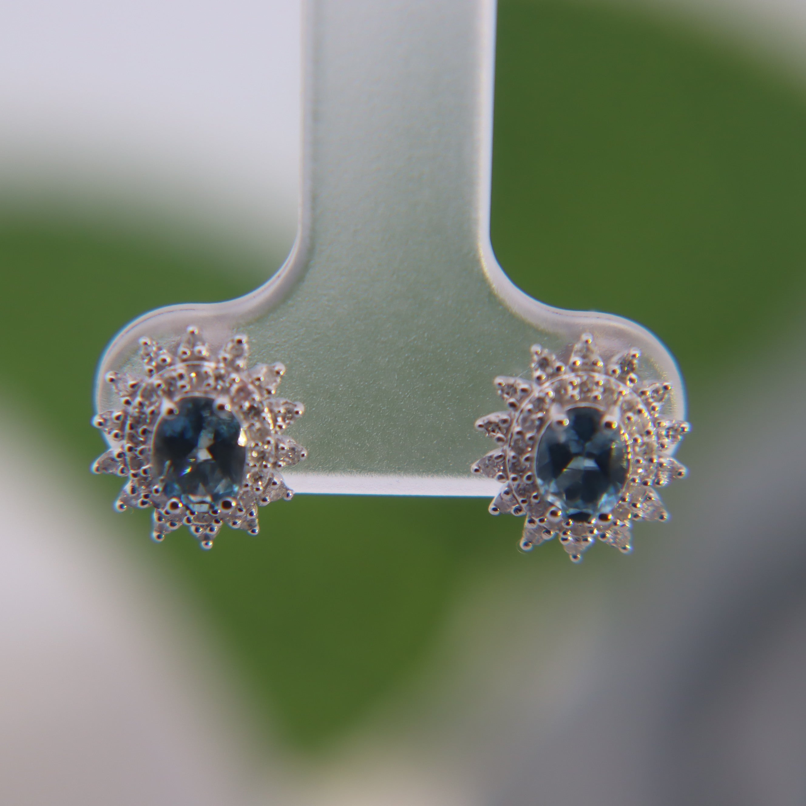 14K White Gold 1/4CT. Diamond & Aquamarine Starburst Earrings on a clear display with a blurred green outdoor background.