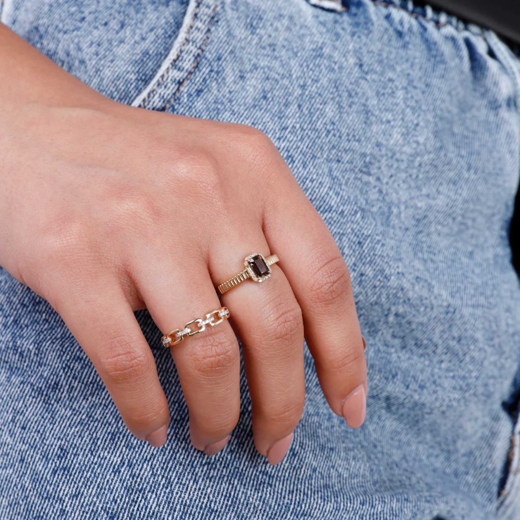 Hand wearing two gold rings with a blue denim background