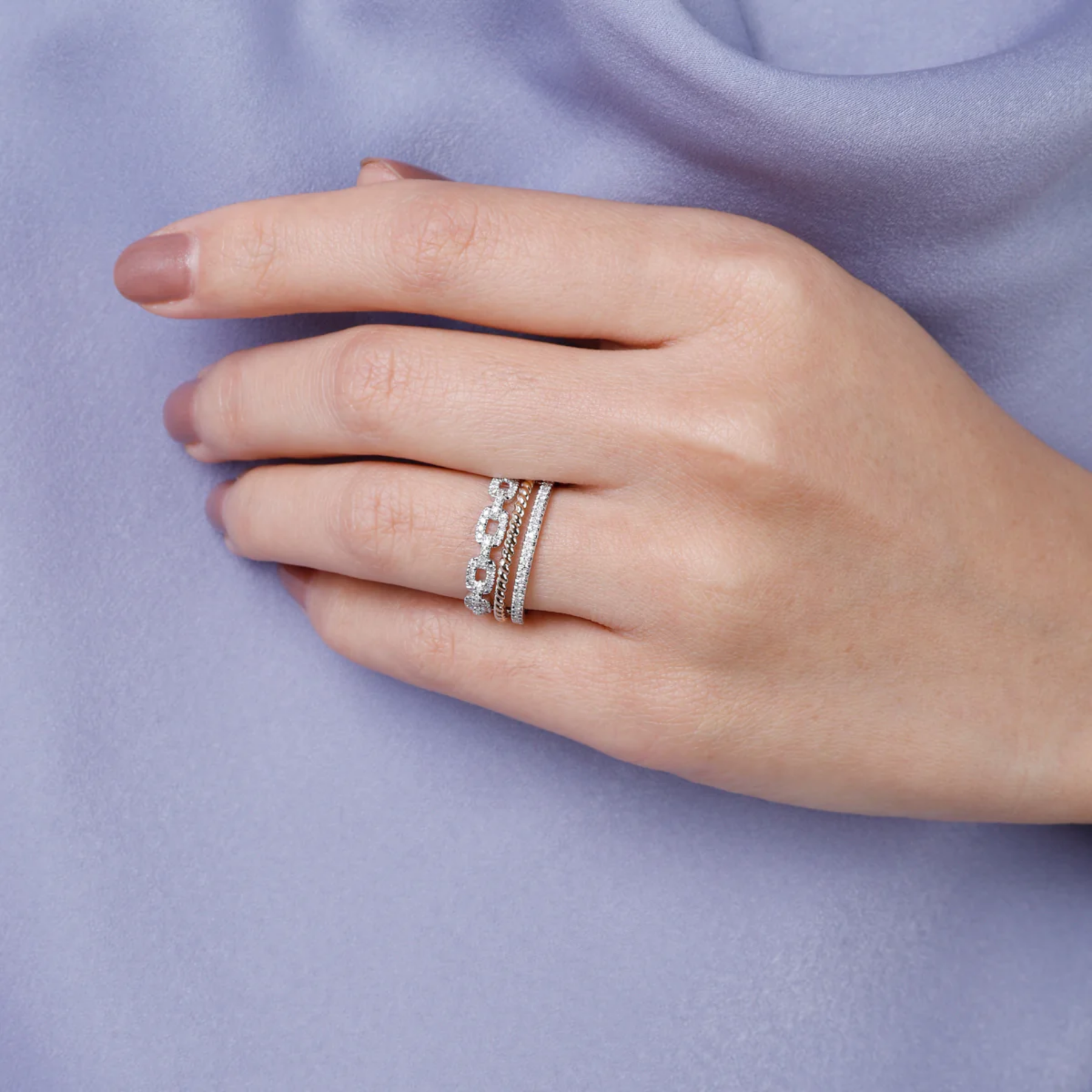 Hand wearing multiple silver rings on a light purple fabric background