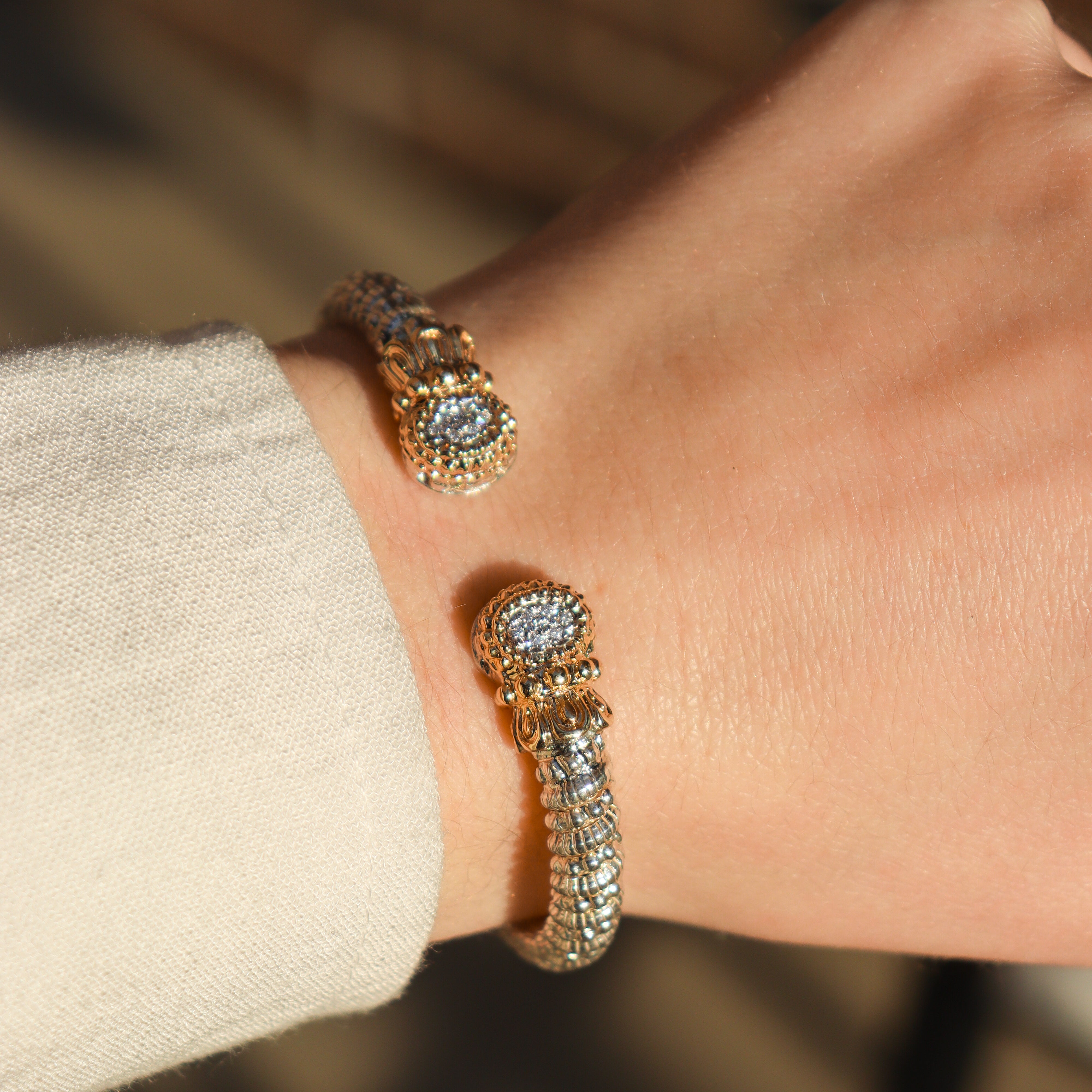 Close-up of a wrist wearing two gold and diamond bracelets against a neutral background.