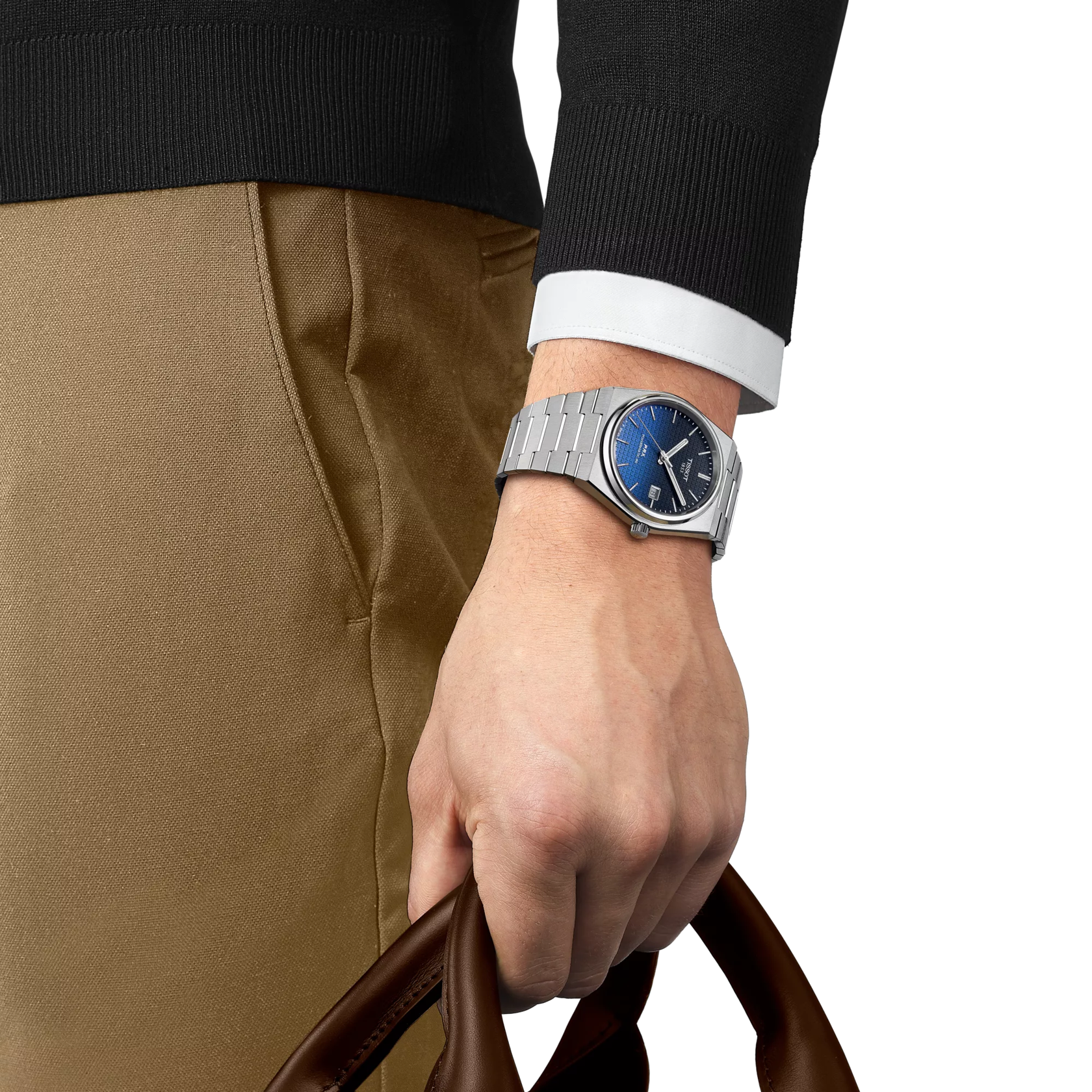Hand wearing a silver watch with a blue face, holding a brown leather bag on a white background.