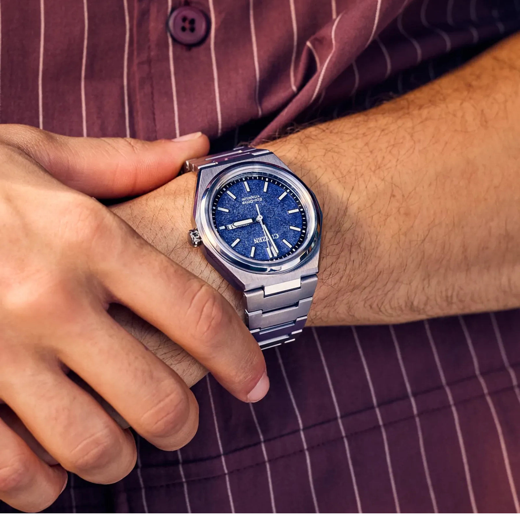 Close-up of a person wearing a silver watch with a blue face on a matching striped shirt.