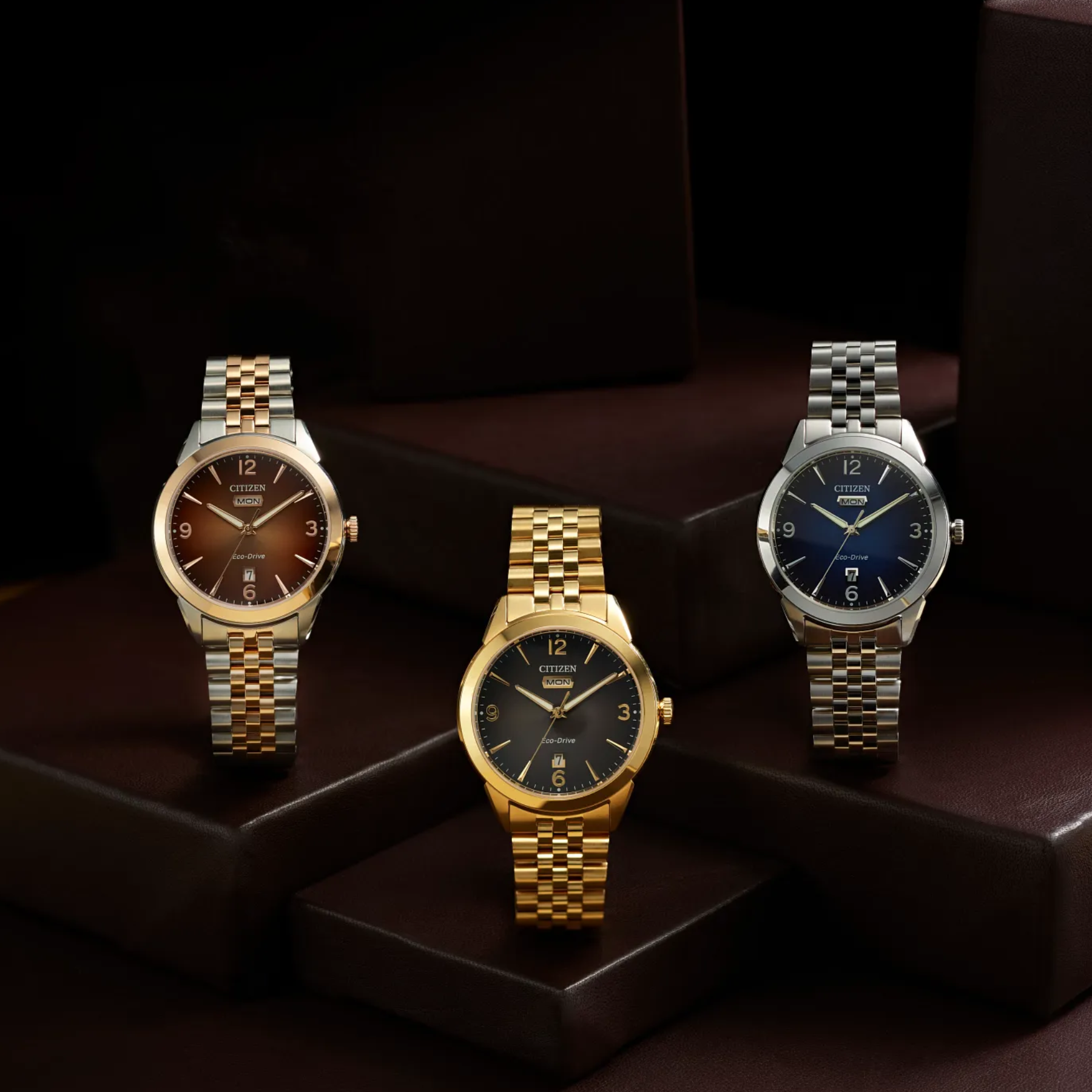 Three watches with different colored faces and metallic bands on a dark background