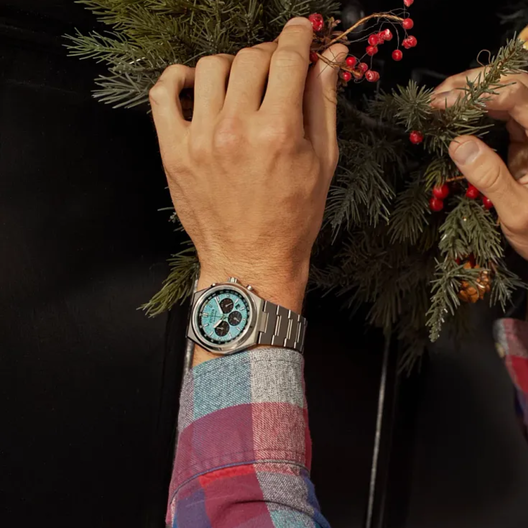 Hand wearing a watch with a decorative wreath on a dark background
