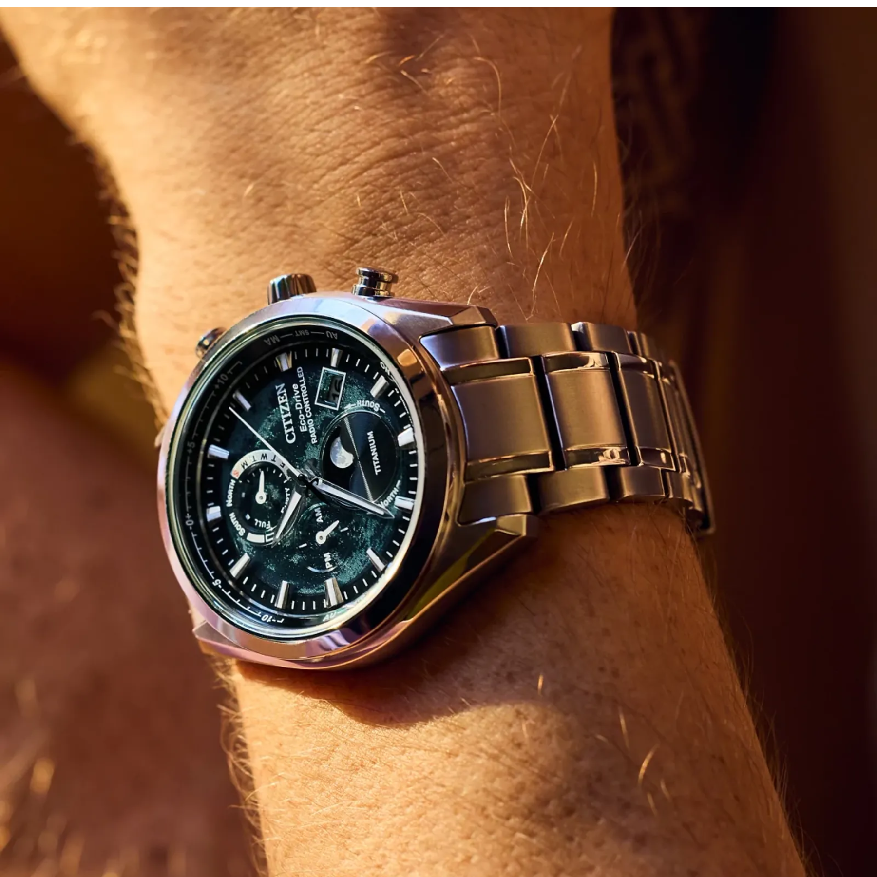 Silver wristwatch with a dark face on a person's wrist, against a blurred background.