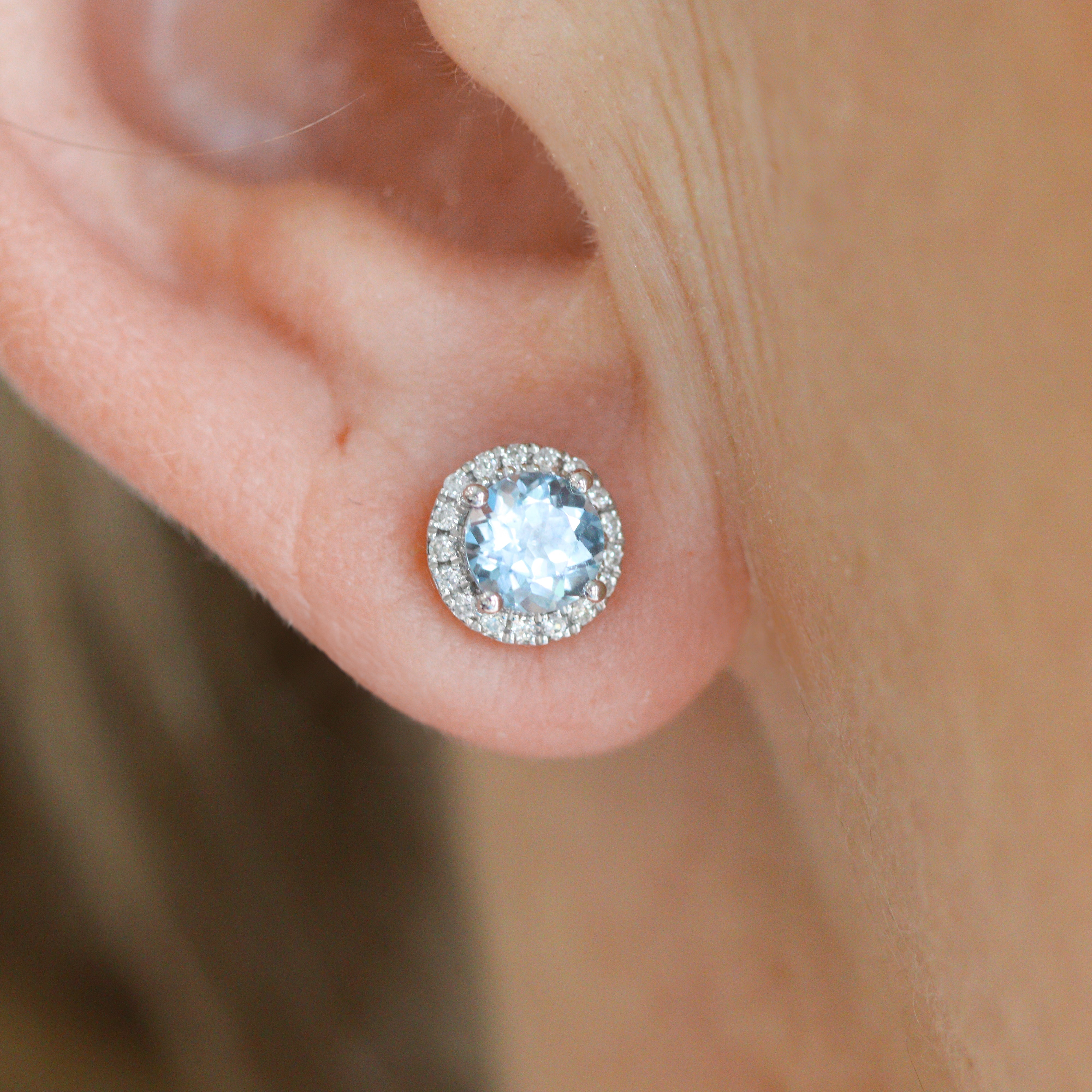 One 14K White Gold 1CTW. Sky Blue Topaz & 1/6CT. Diamond Halo Stud Earring on a model's ear, close up.