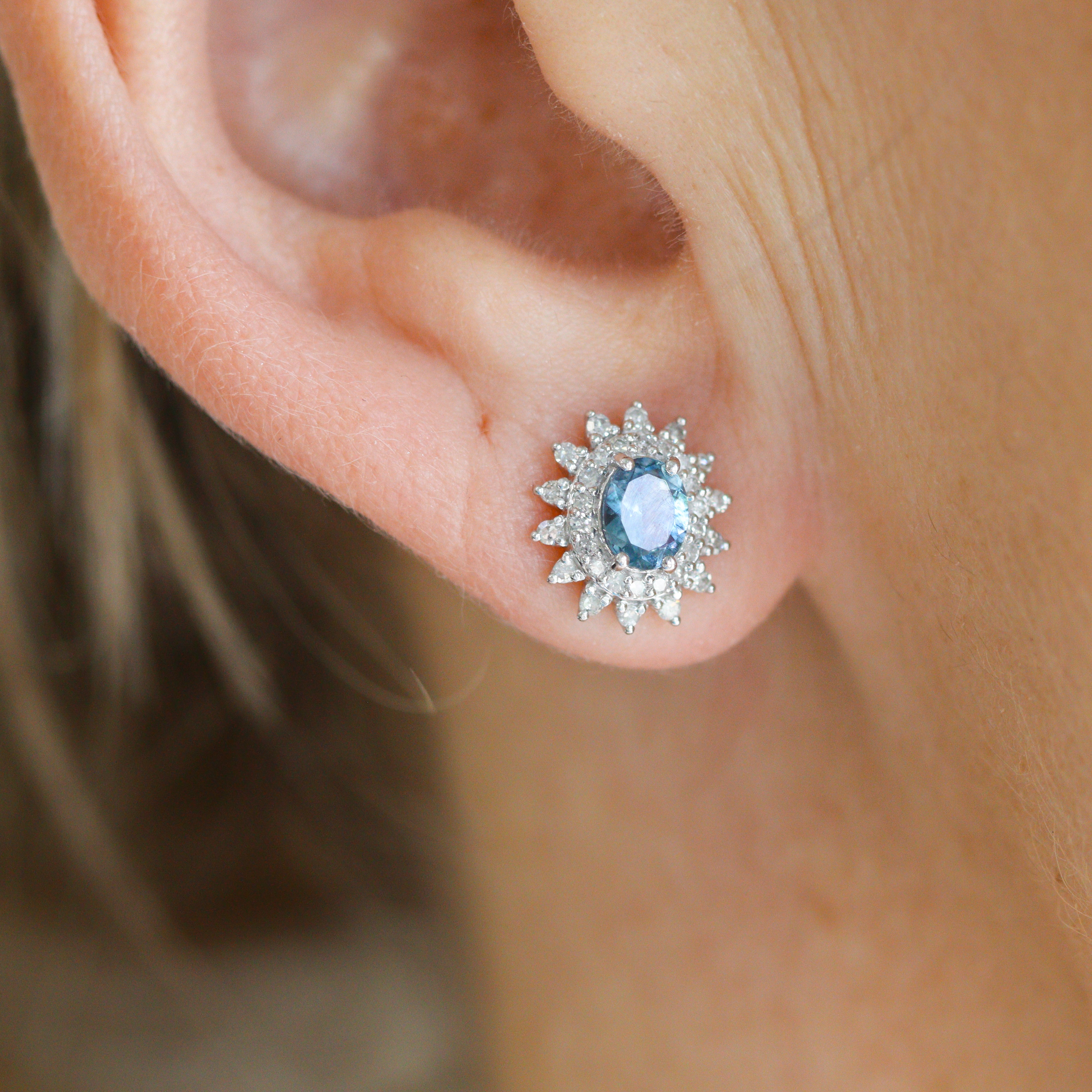 One 14K White Gold 1/4CT. Diamond & Aquamarine Starburst Earrings on a model's ear, close up.