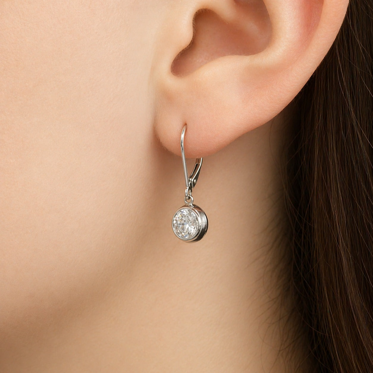 Silver earring with a round gemstone worn on an ear against a neutral background