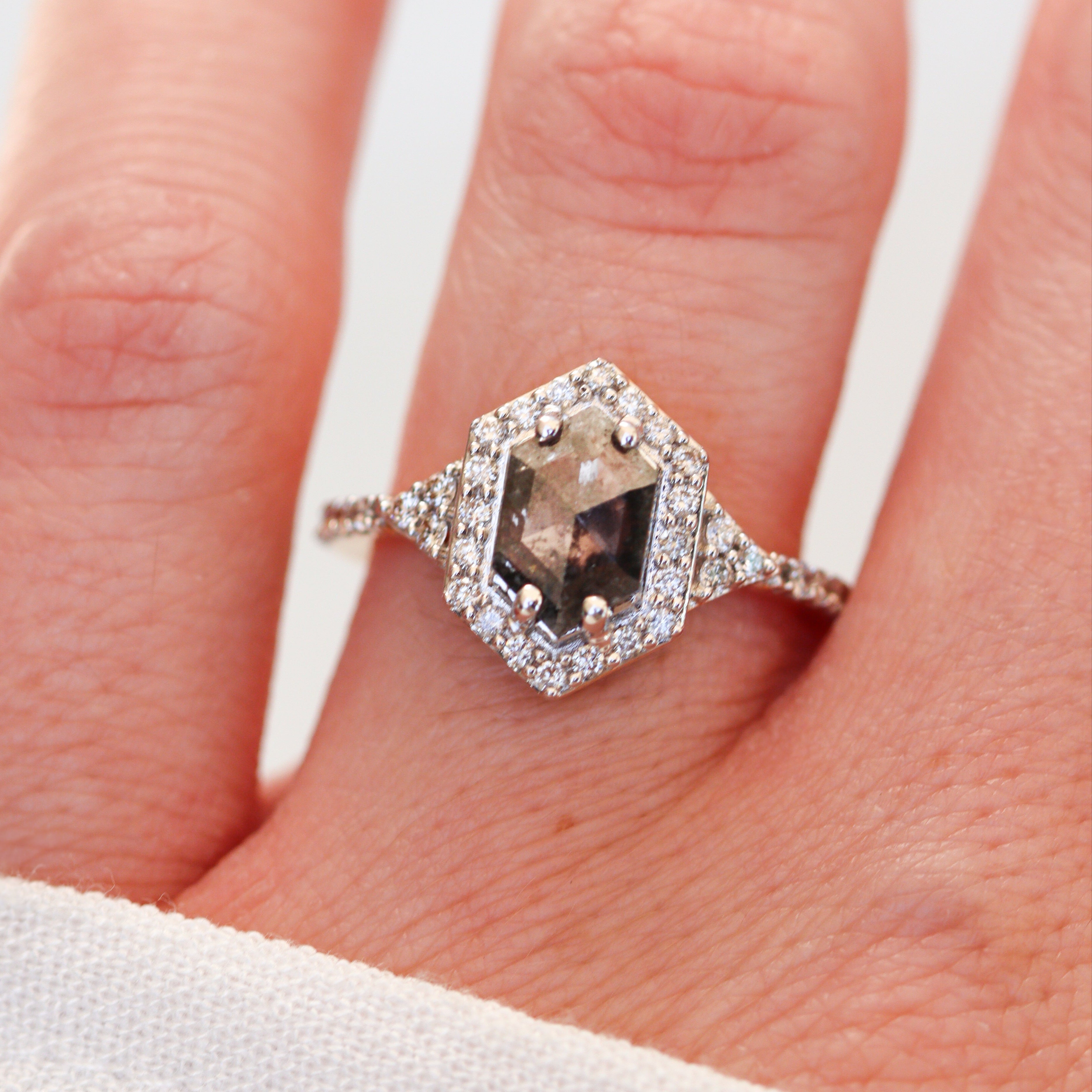 Ring with a central diamond and smaller diamonds on a finger against a white background