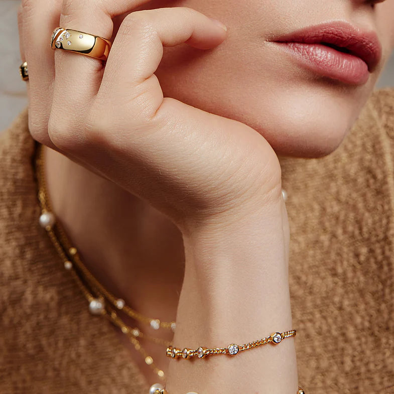 Close-up of a hand wearing a gold ring and bracelet against a neutral background
