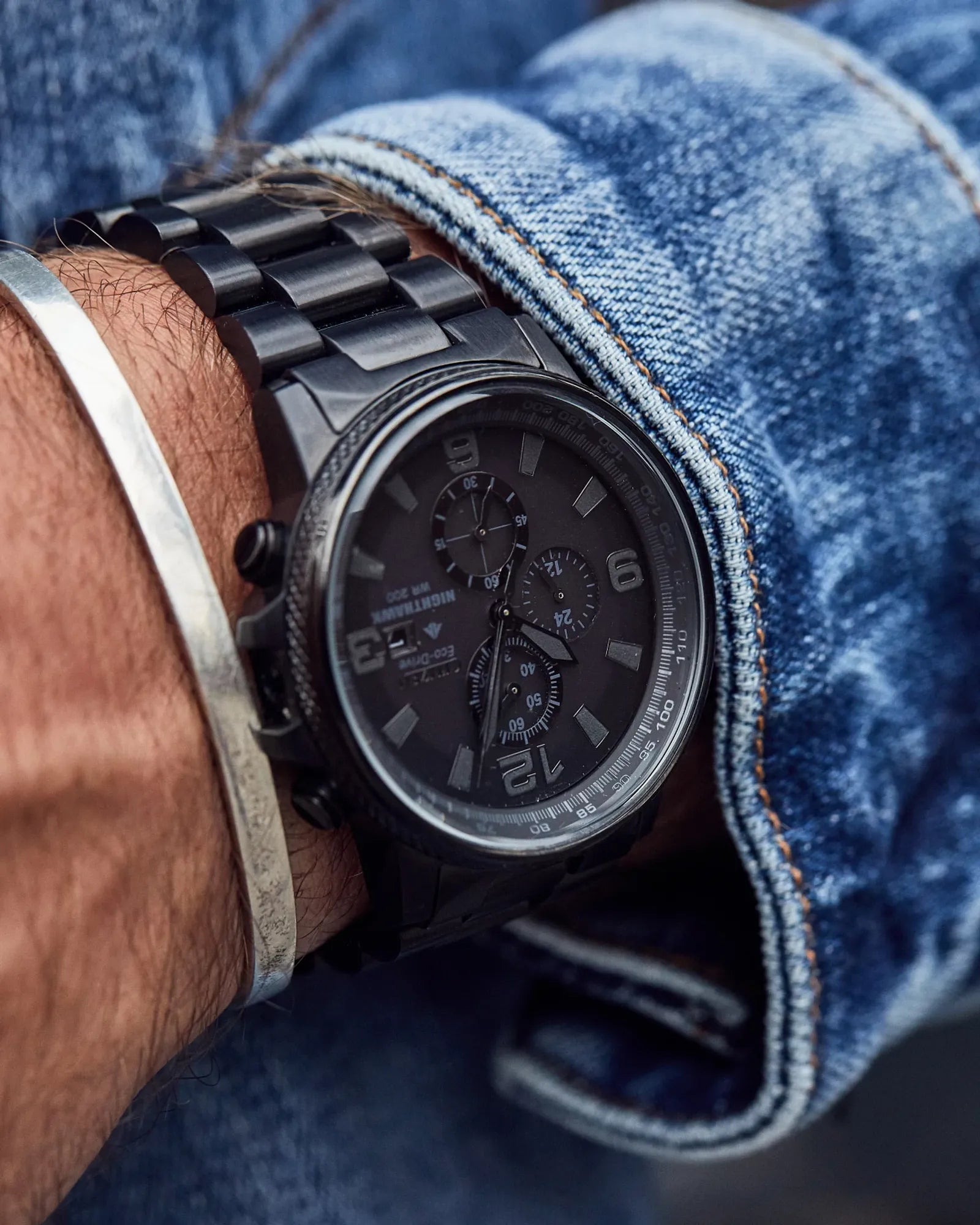 Black wristwatch on a person's wrist with blue jeans