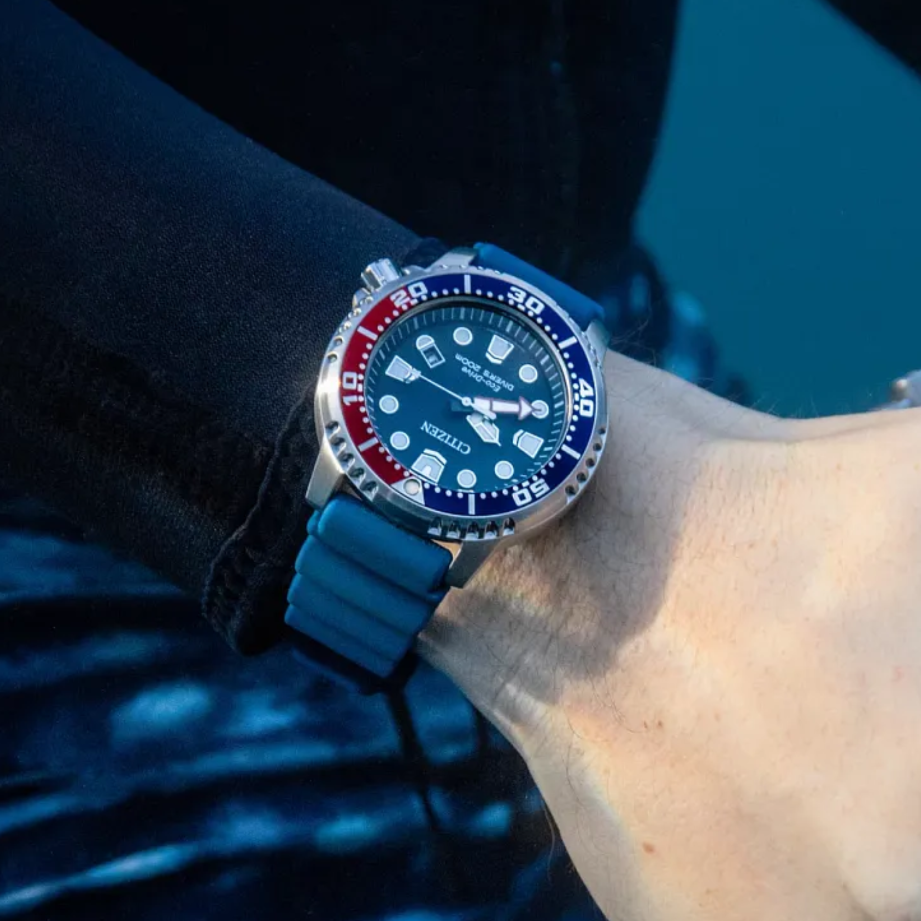 Blue watch with a red and white bezel on a wrist against a dark background