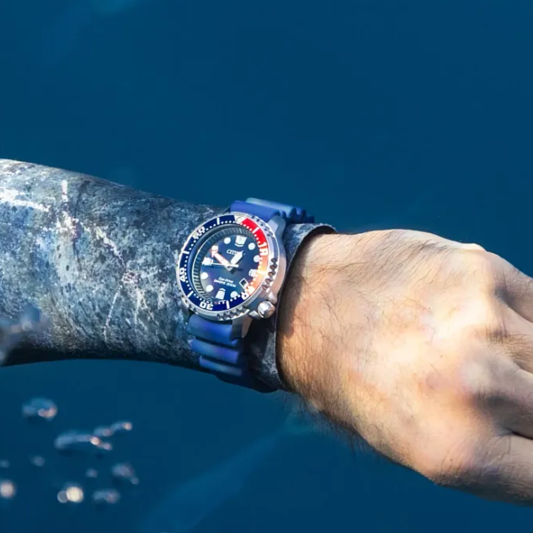 Person wearing a blue diving watch underwater with a blue background