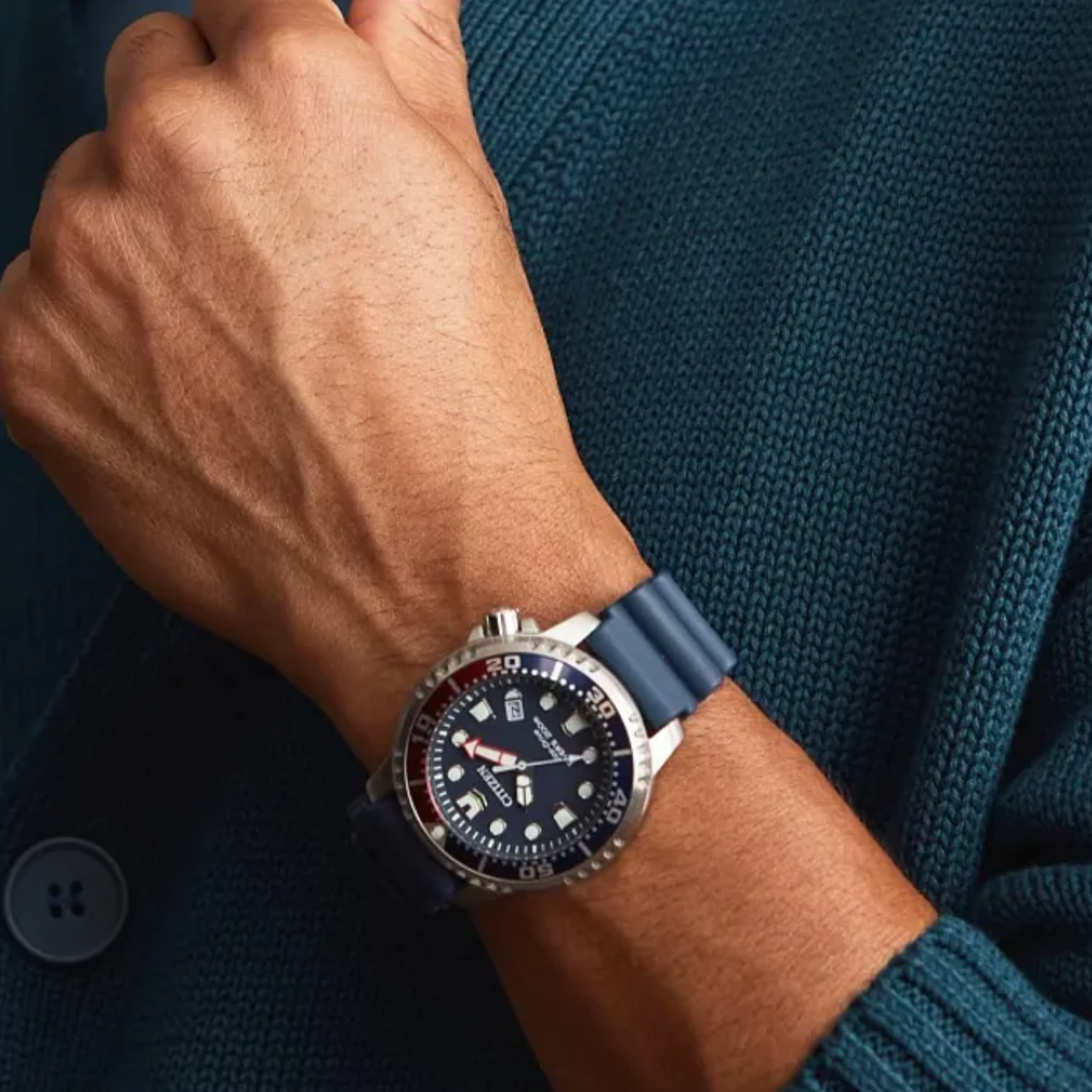 Close-up of a wrist wearing a watch with a blue strap against a teal sweater background