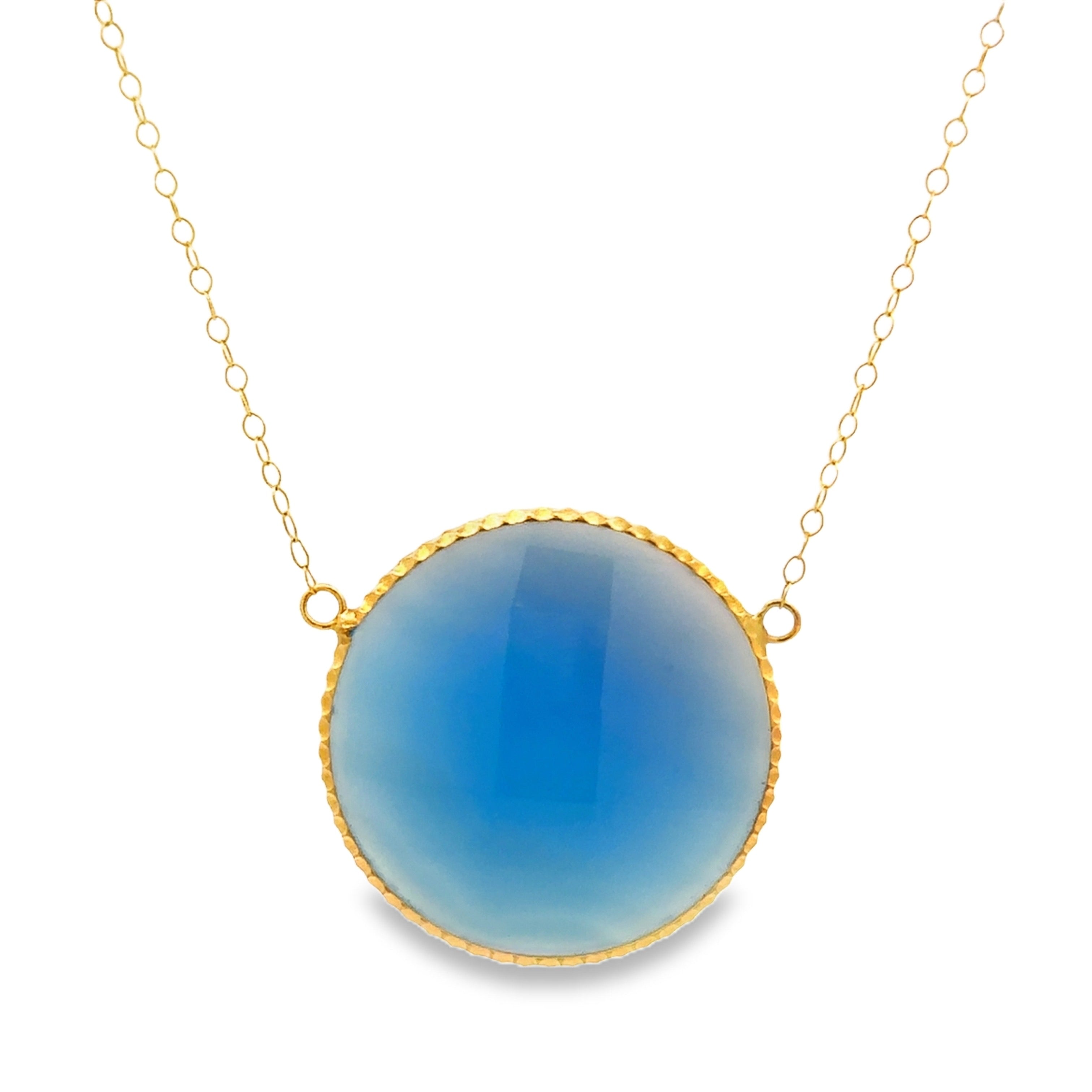 A gold chain necklace featuring a large, round cabochon pendant with a smooth blue gradient center and a textured gold bezel, set against a plain white background.