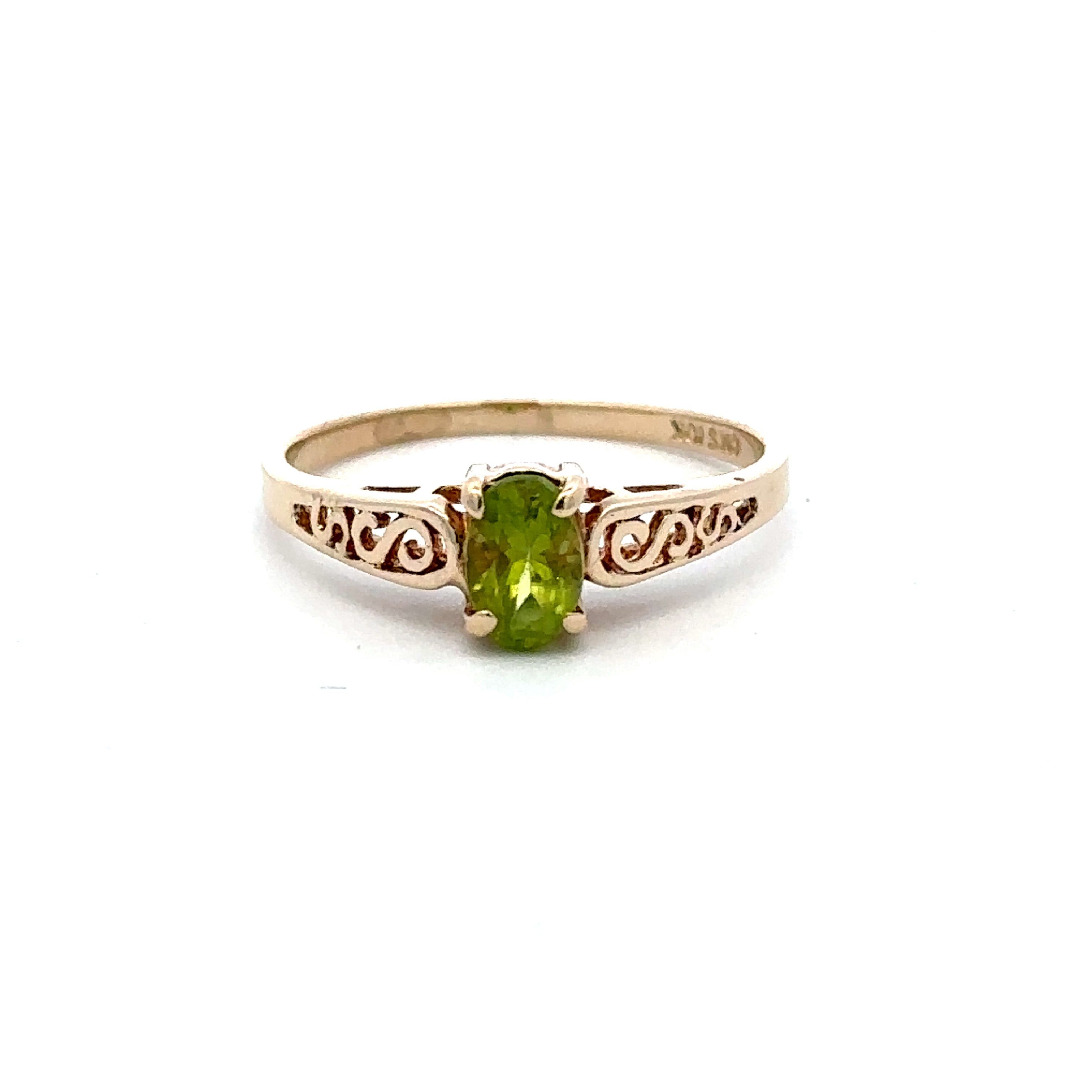 A yellow gold ring featuring an oval-cut green peridot gemstone in a prong setting, with decorative scrollwork on the band, shown against a plain white background.
