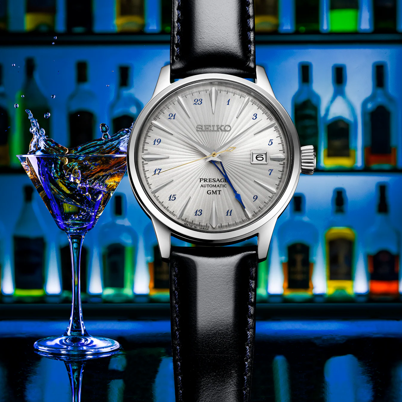 Seiko watch with a black leather strap next to a cocktail glass with water splashing, against a colorful bottle background.
