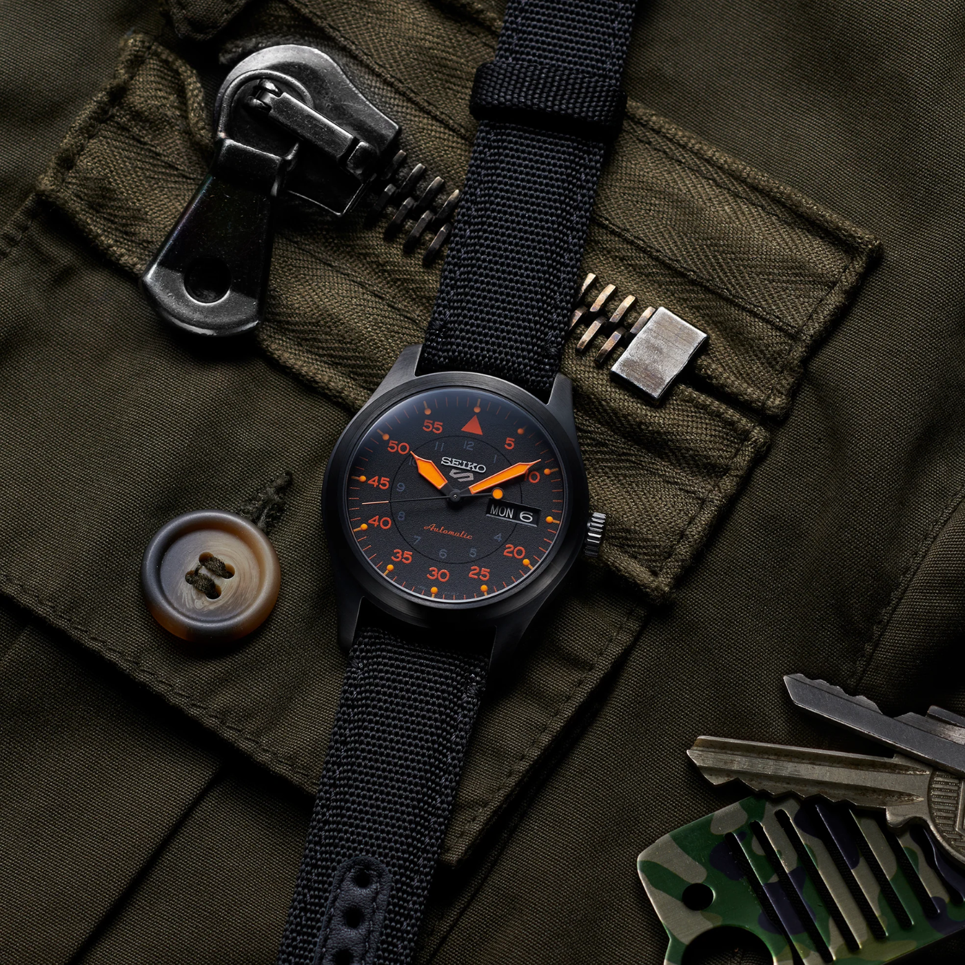 Black Seiko watch on a green military-style jacket with tools and equipment.