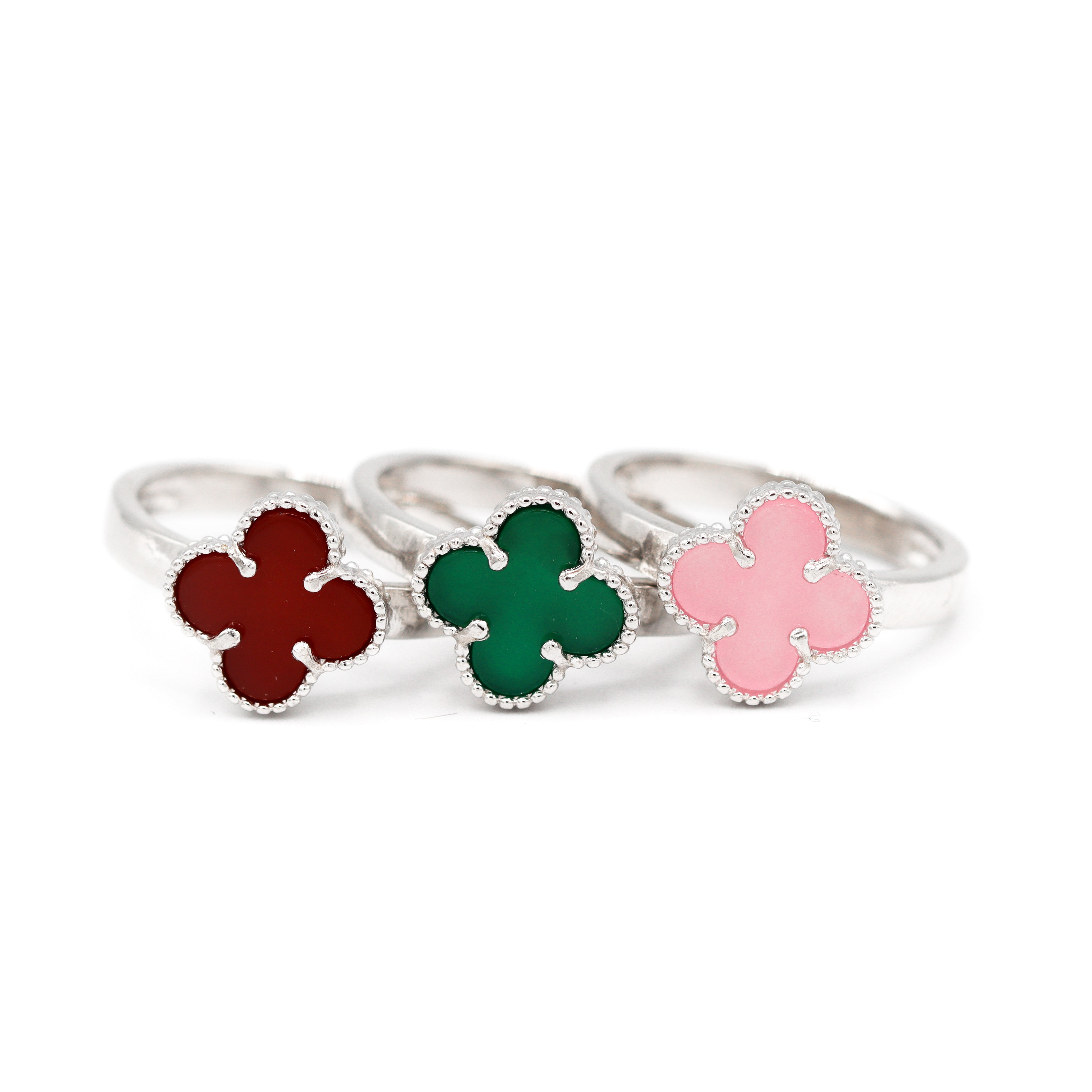 3 Rings, each with one clover shaped stone in the middle. One is red, one is green, and one is pink.