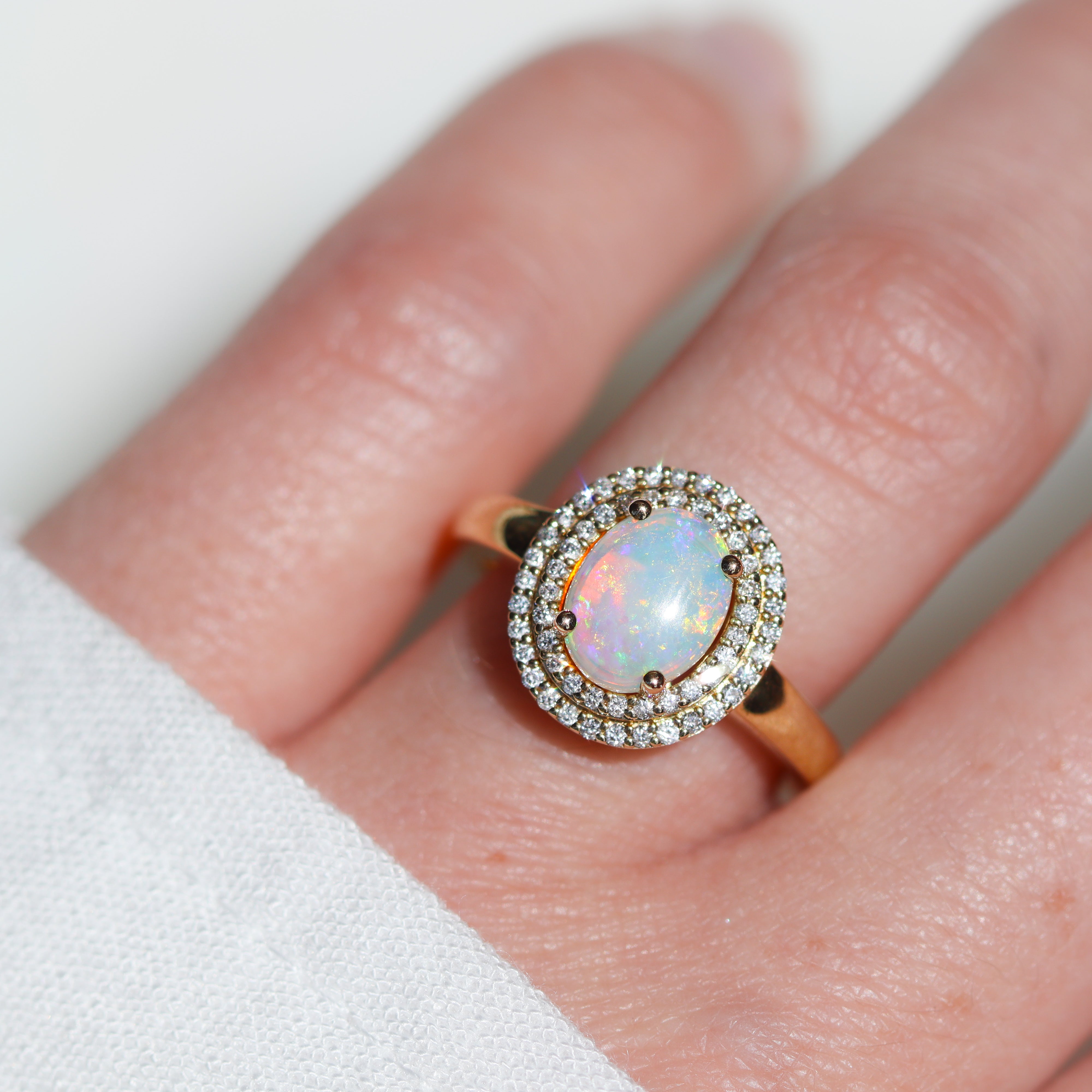 Top view of 14K Yellow Gold 1CT. Opal & 1/4CT. Diamond Double-Halo Engagement Ring on model's hand in the sunlight.