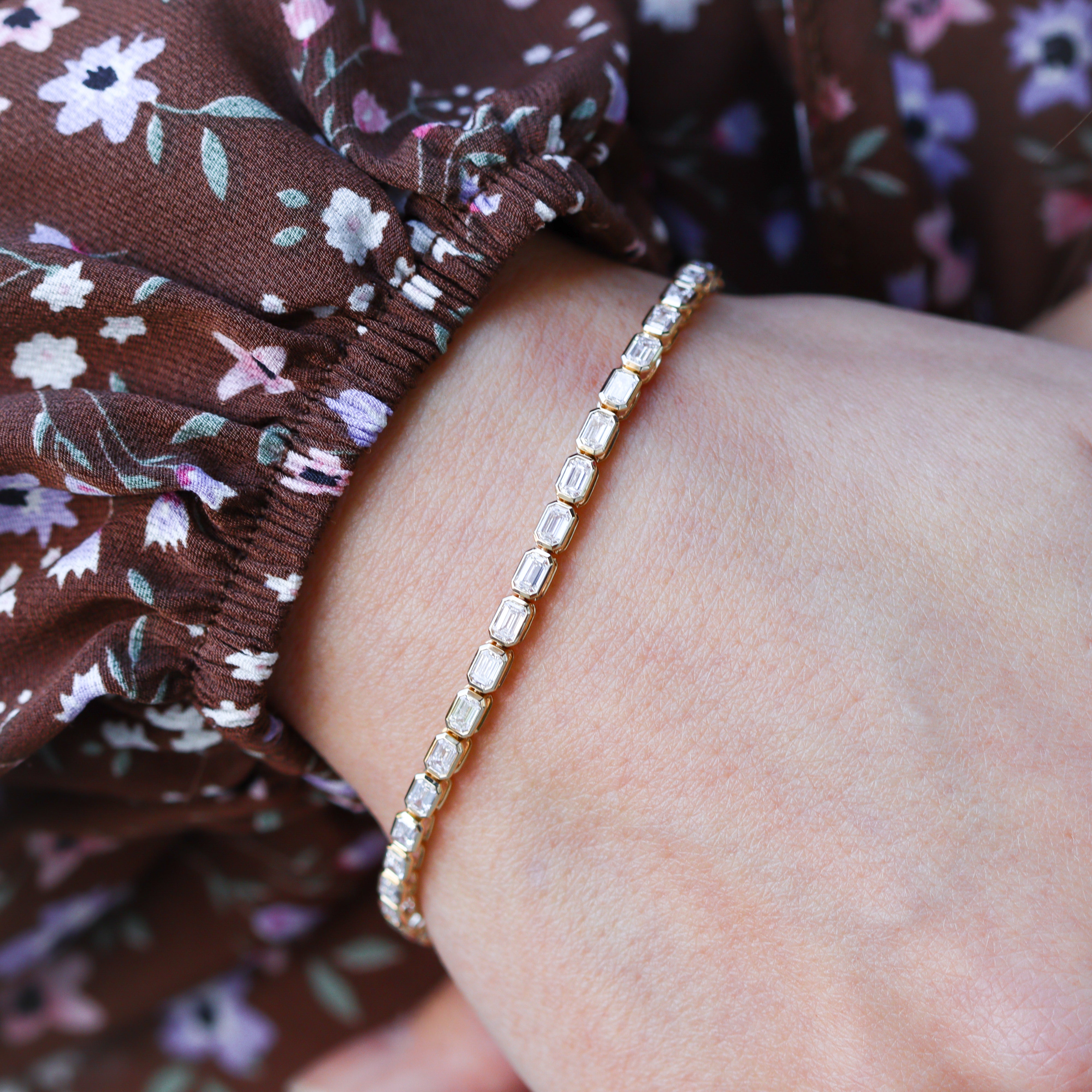 Zoomed in image of tennis bracelet on a model's wrist who is wearing a floral dress.