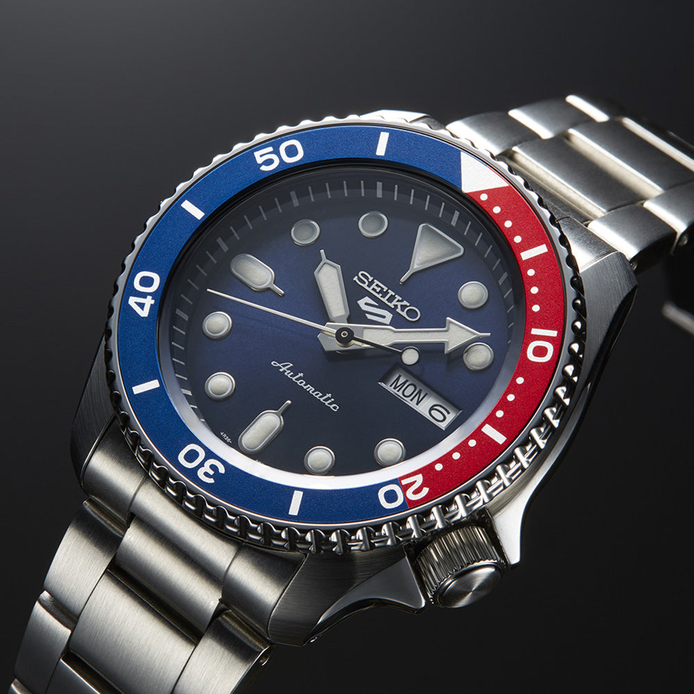Angled close-up of the Seiko SRPD53 blue dial, luminous hands and hour markers, day-date window and red-and-blue bezel.