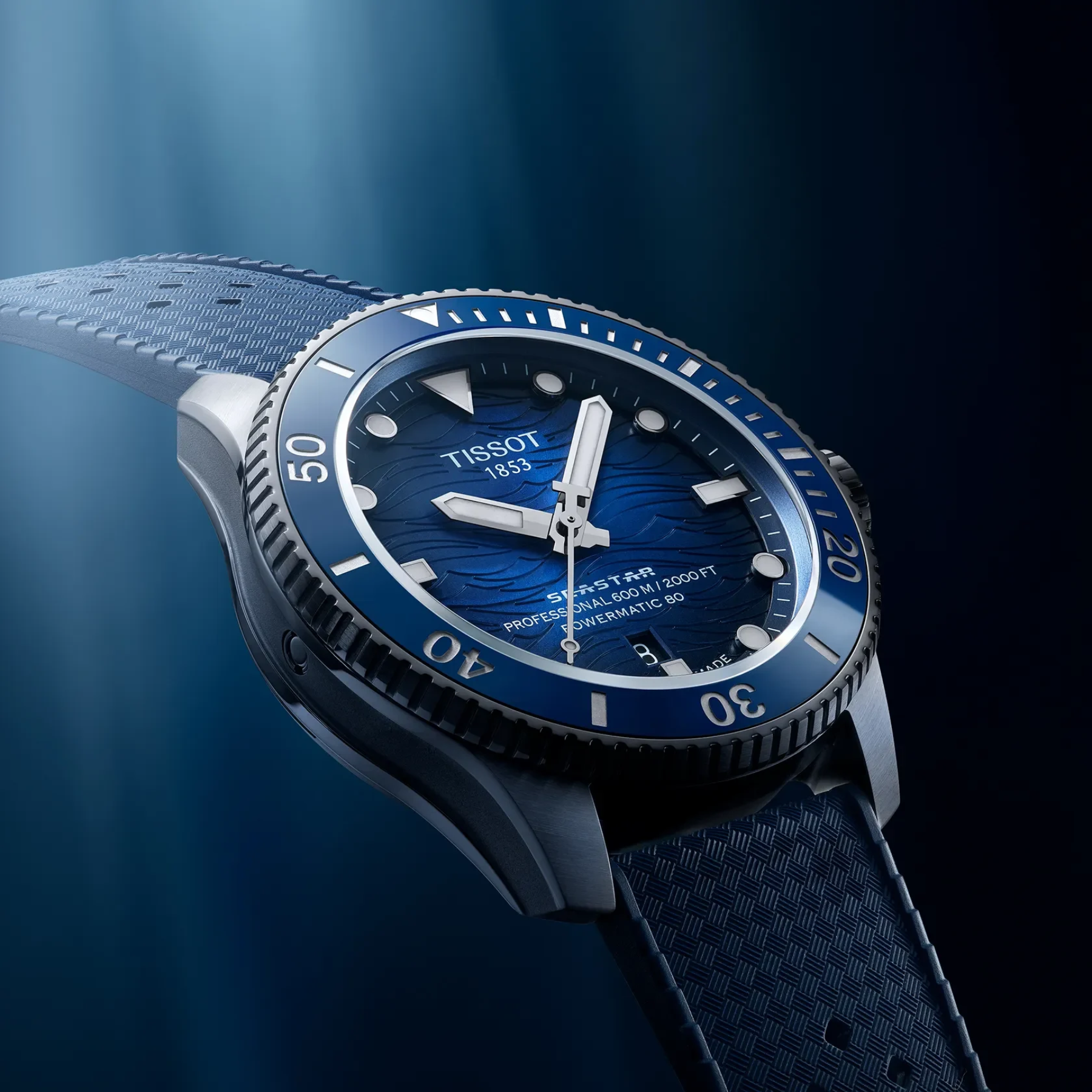 A Tissot 1652 watch with a blue sunburst dial, silver-tone case, and textured blue strap, shown at an angle against a dark blue background with soft light rays.