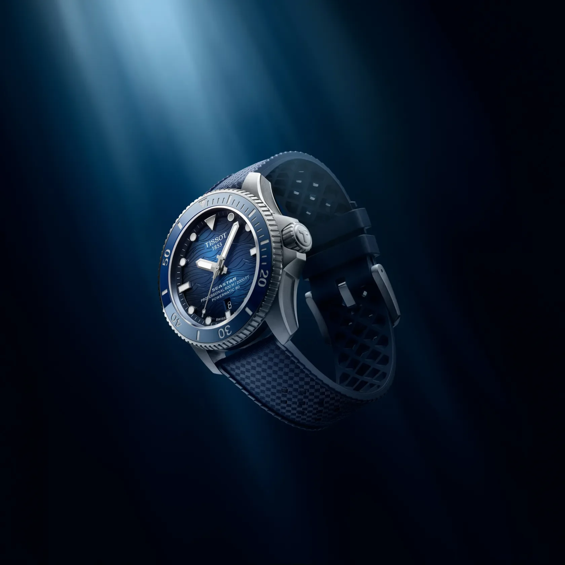 A wristwatch with a dark blue dial, blue bezel, and textured dark strap, shown floating against a dark blue background with dramatic light rays.
